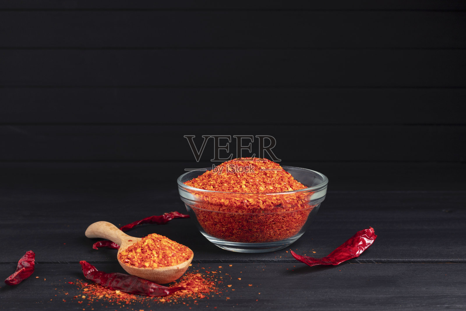 碗中放着辣椒粉、干辣椒和辛辣调料，背景为深色桌面。照片摄影图片