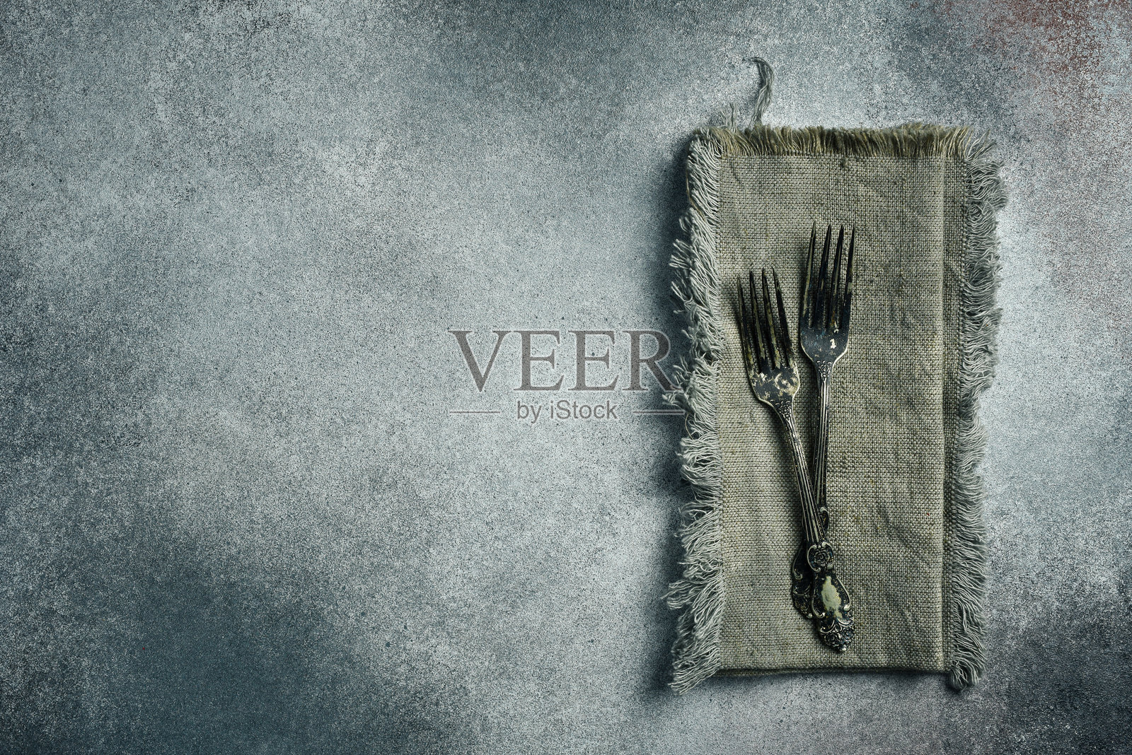 旧式复古餐叉放在亚麻毛巾上。背景为灰色混凝土，特写镜头。照片摄影图片