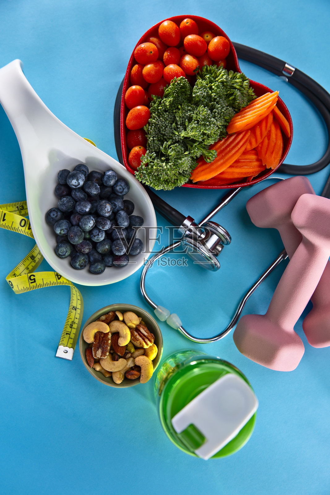 蓝色背景下，心形碗中的蔬菜，旁边有哑铃和蓝莓照片摄影图片