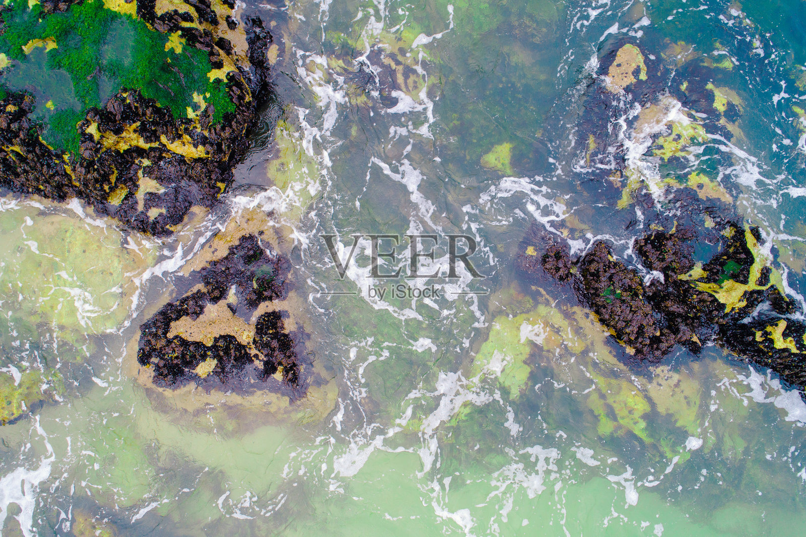 海滩岸边苔藓岩石上的海浪拍打，航拍俯视图照片摄影图片