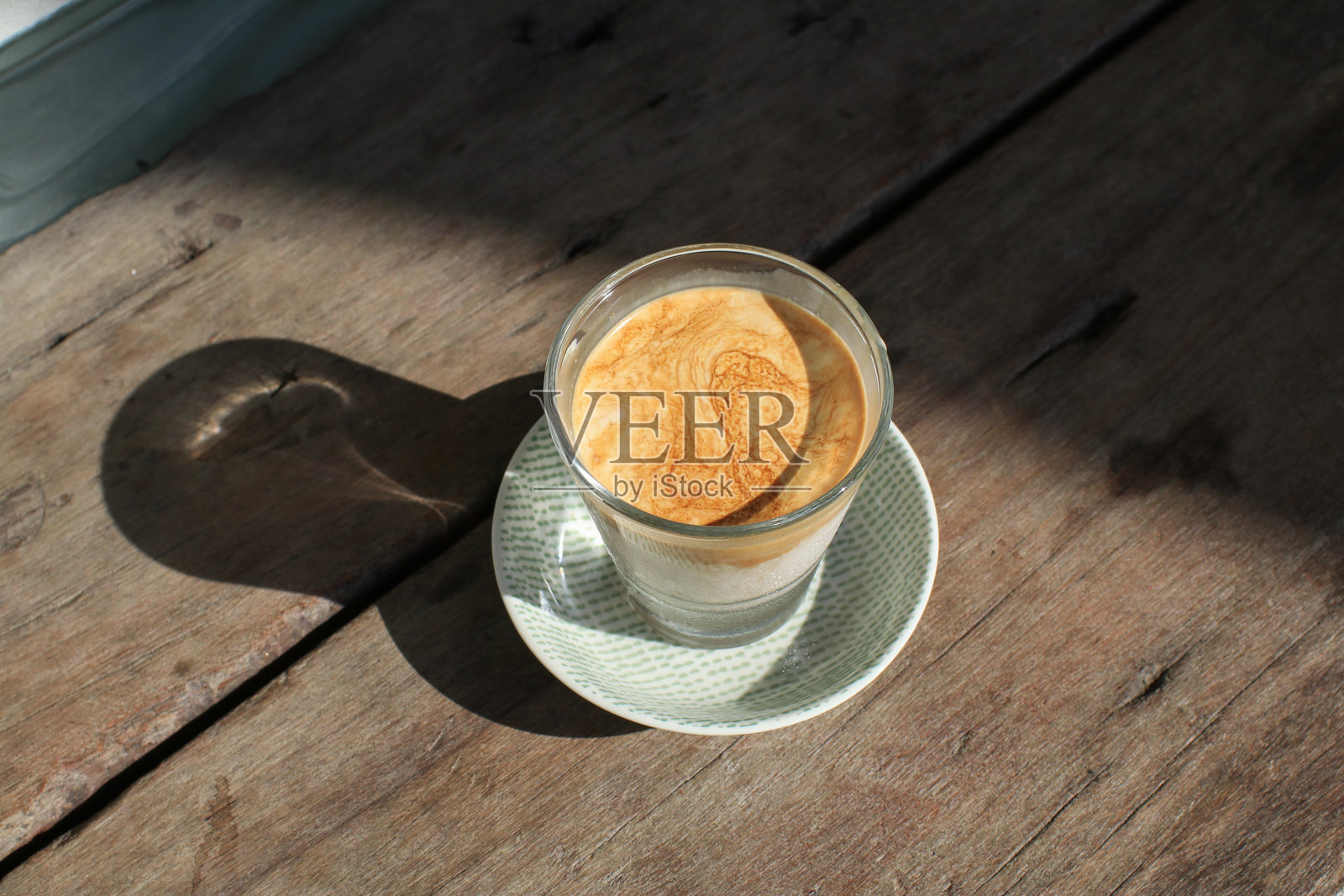 阳光和阴影下，木板上盛着脏咖啡拿铁的玻璃杯。顶部是浓缩咖啡层，底部是冰冷的牛奶或奶油。照片摄影图片