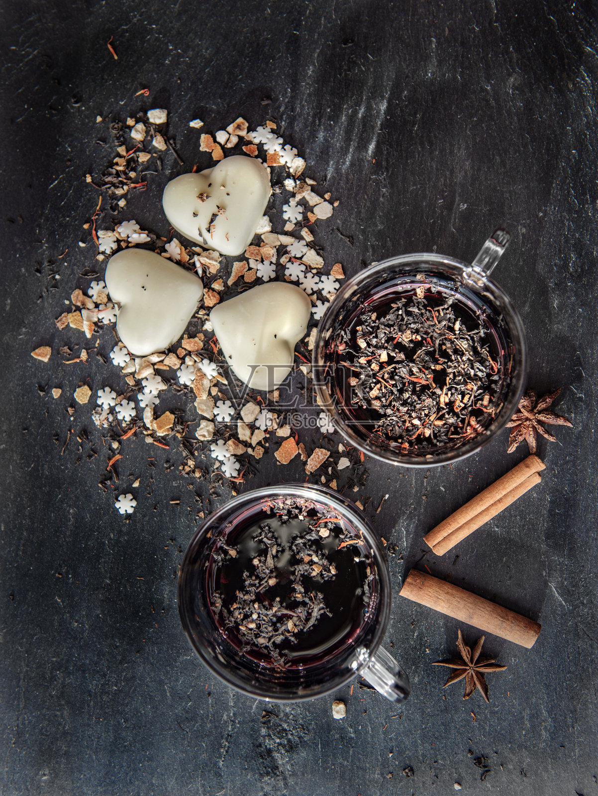 从上方俯视两杯热红酒，旁边摆放着心形饼干和香料，背景为灰色石板。照片摄影图片