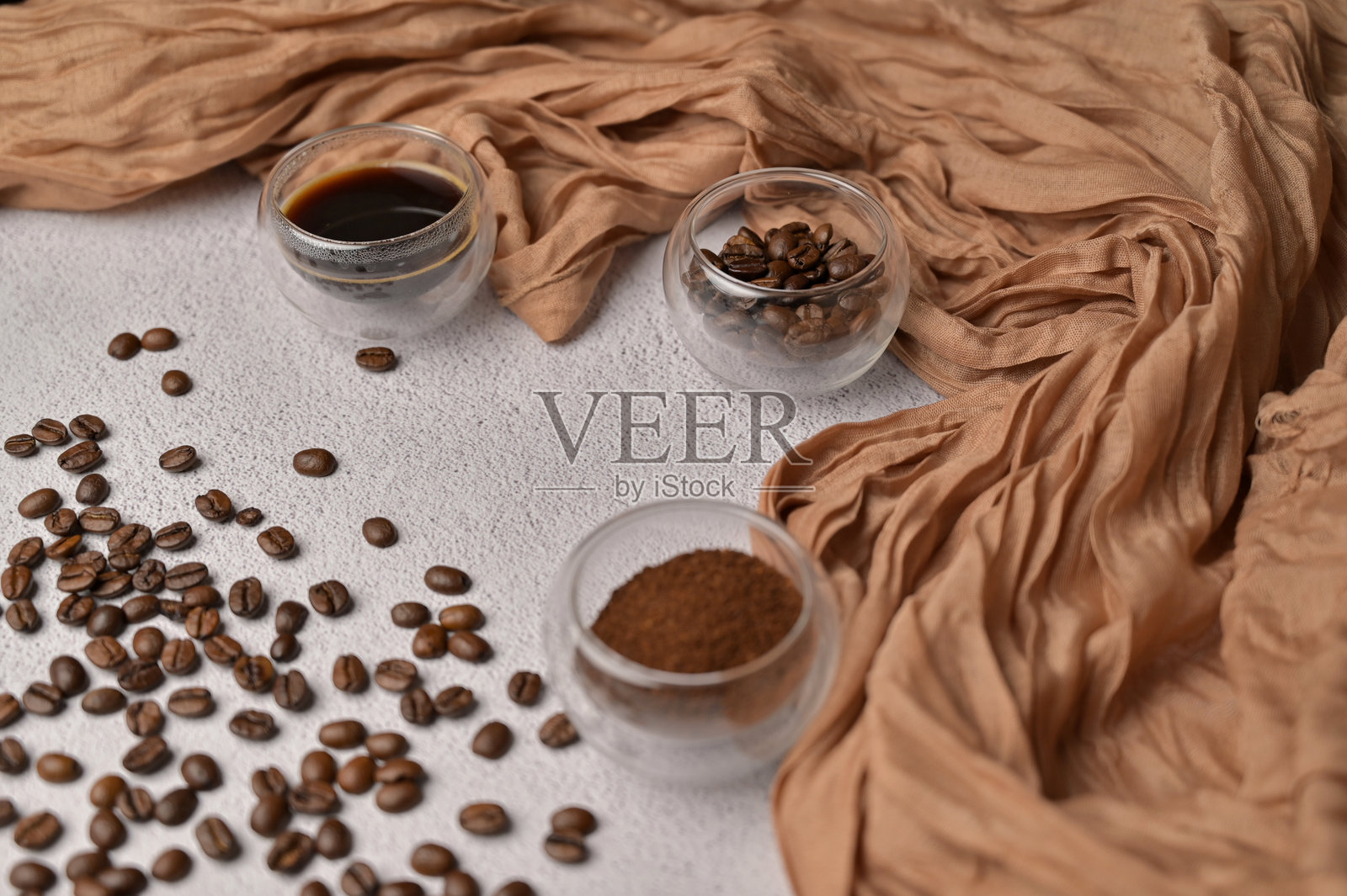 新鲜芳香的谷物，研磨成咖啡饮料，盛在小玻璃杯中，白色背景，棕色布料照片摄影图片