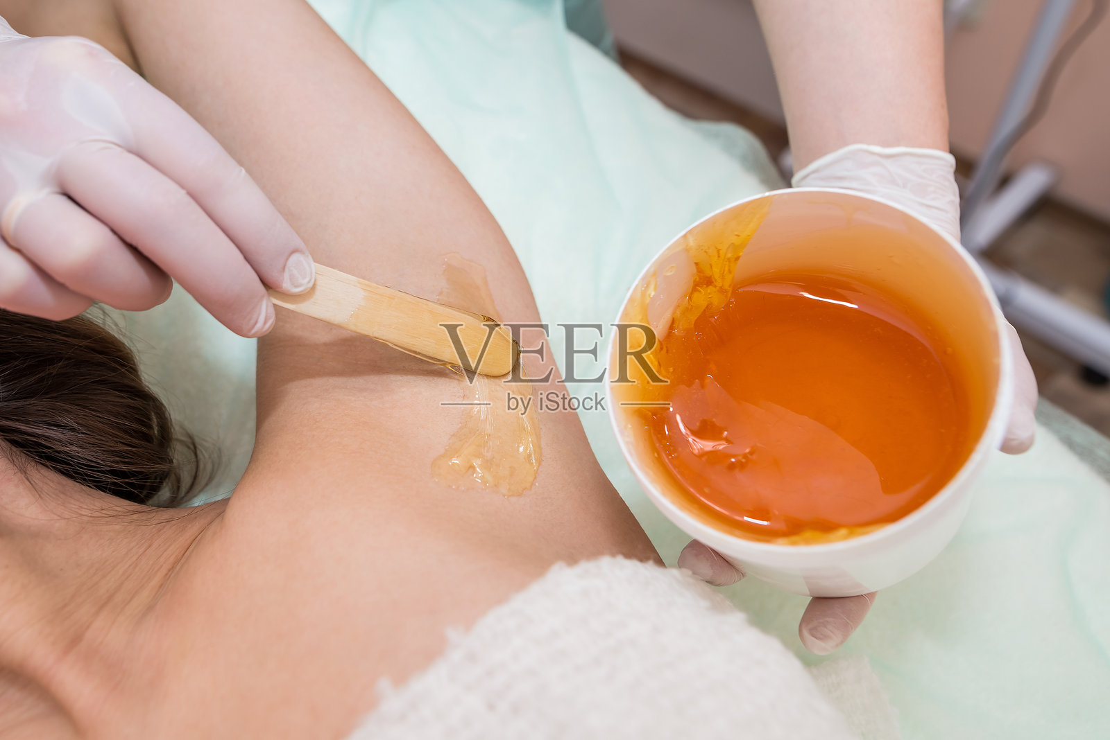 美容师在美容院为腋下进行糖膏脱毛。女性美容护理。照片摄影图片