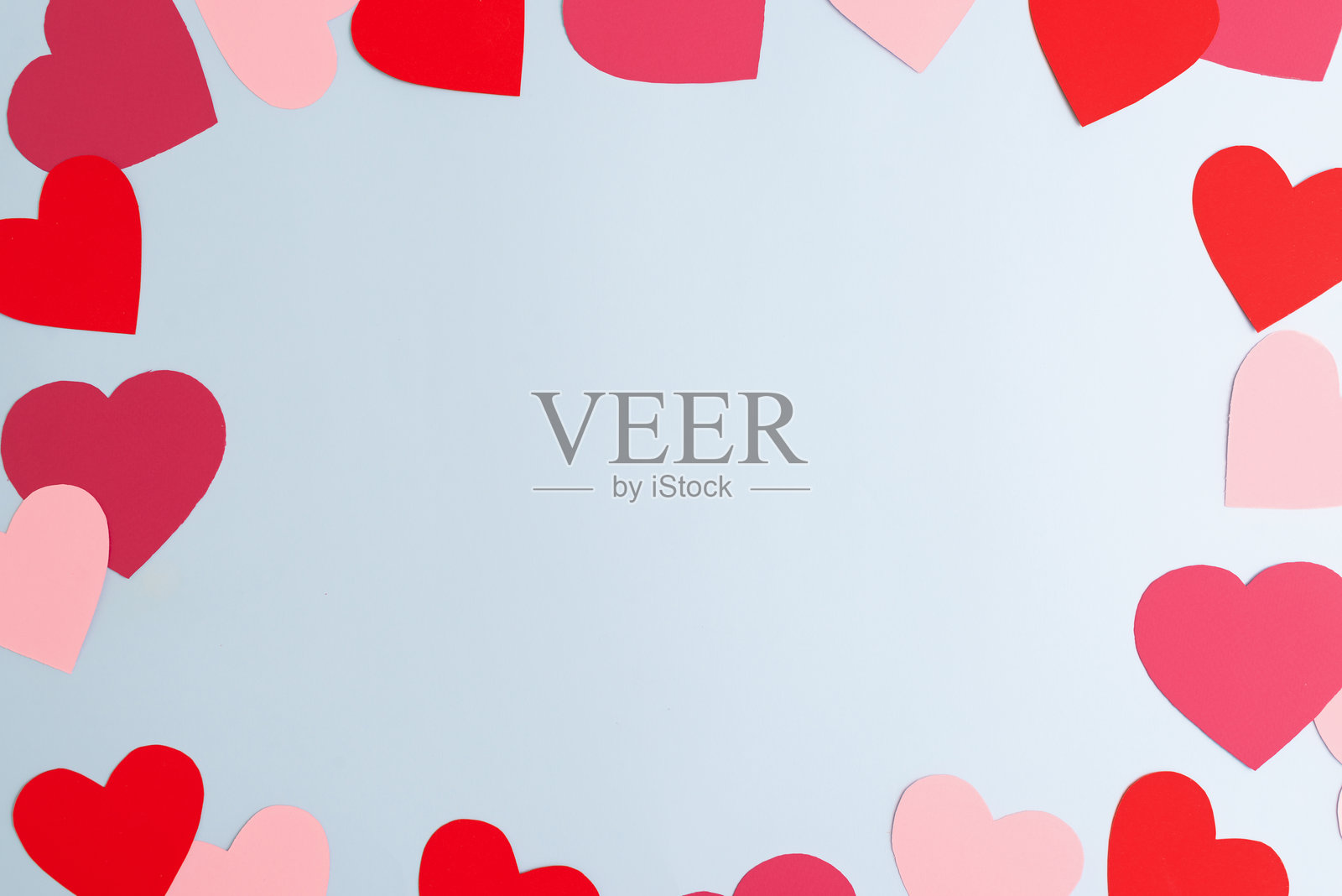红色和粉色的纸心形图案，大小不一，散落在淡蓝色背景上。情人节，爱情和情感的概念。照片摄影图片