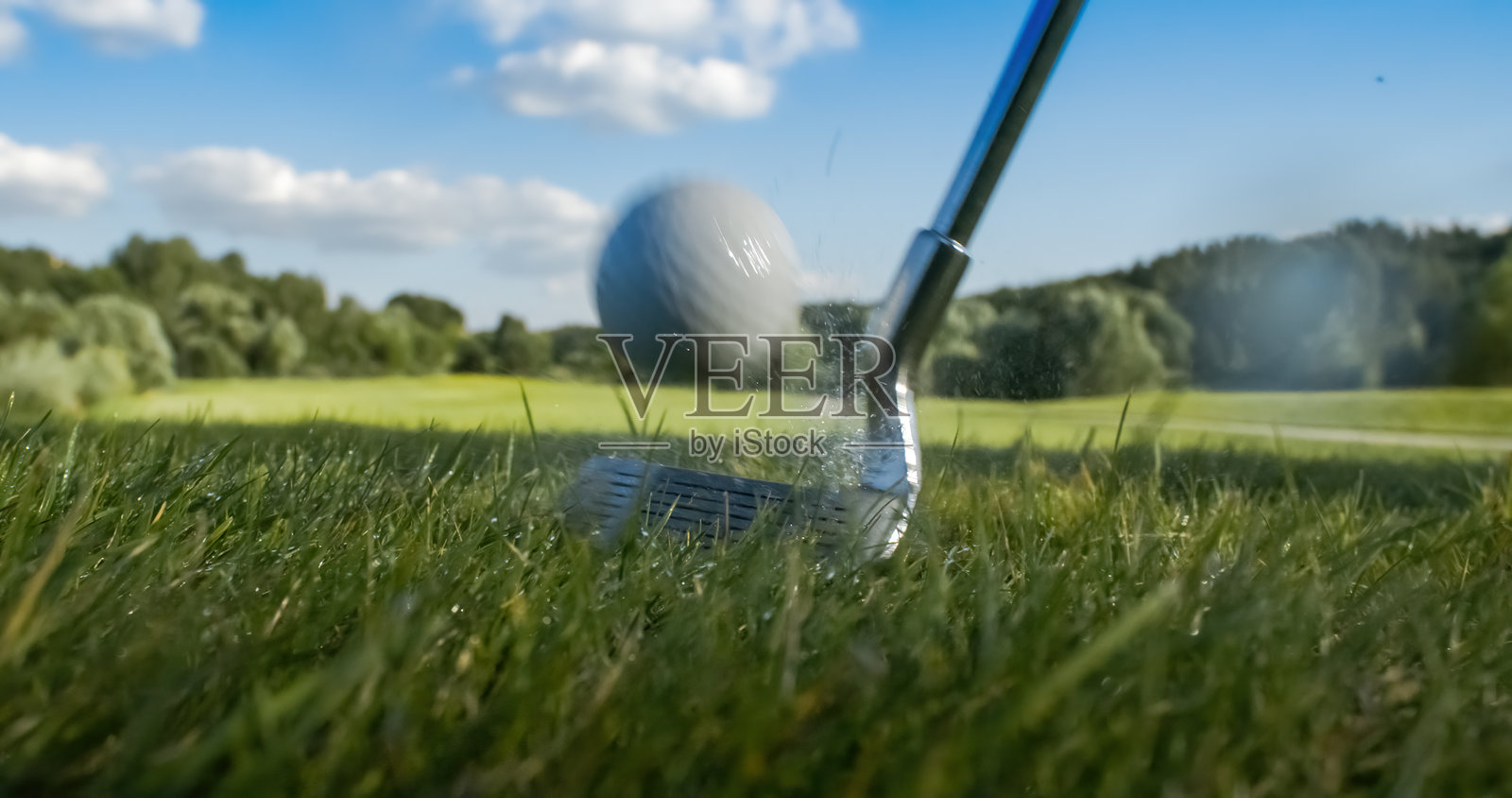 高尔夫球杆击打高尔夫球。晨露和草屑在撞击后飞扬起来。照片摄影图片