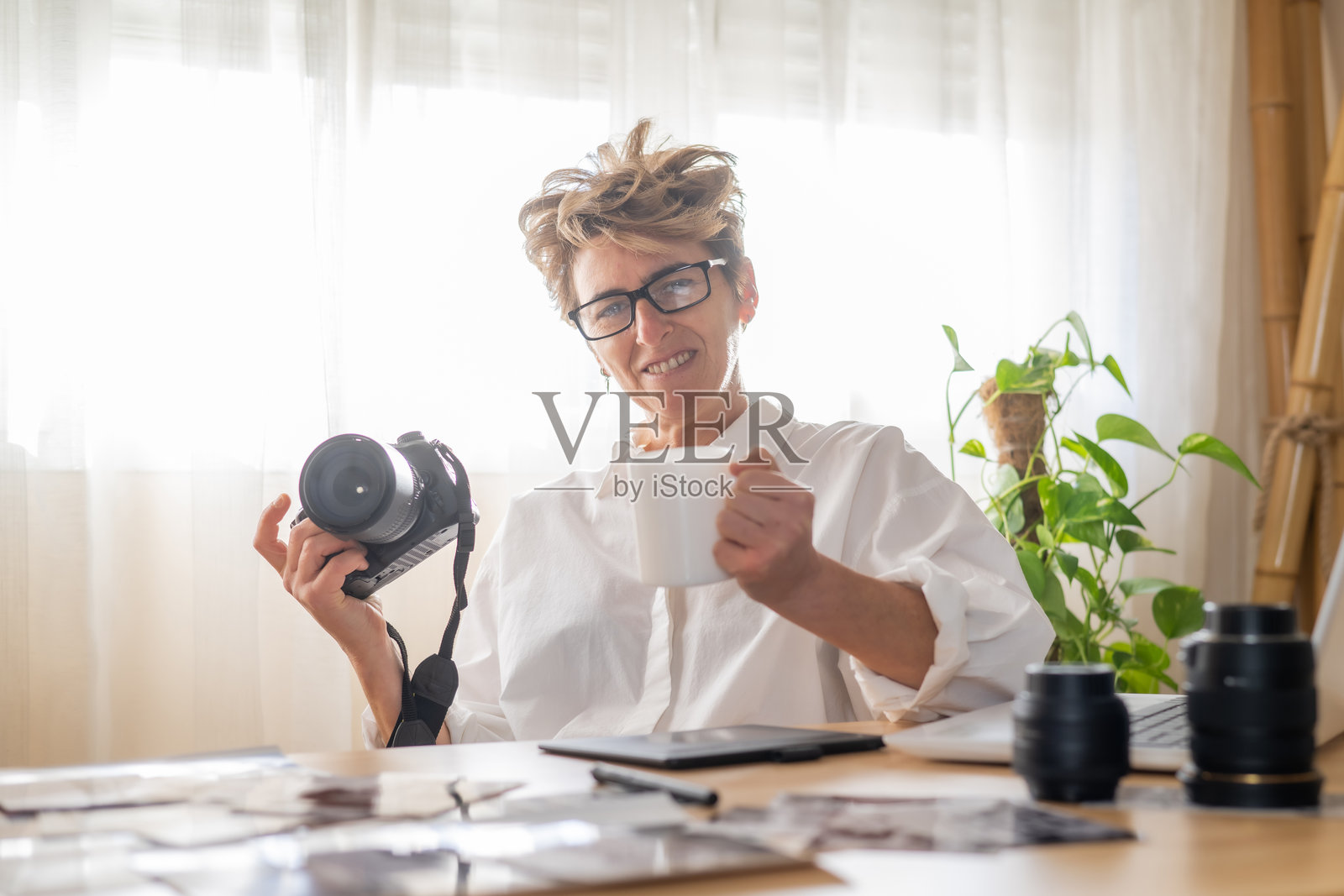 专业摄影师在家中工作空间放松，享用咖啡，周围充满相机设备和照片打印，营造出宁静的工作环境照片摄影图片