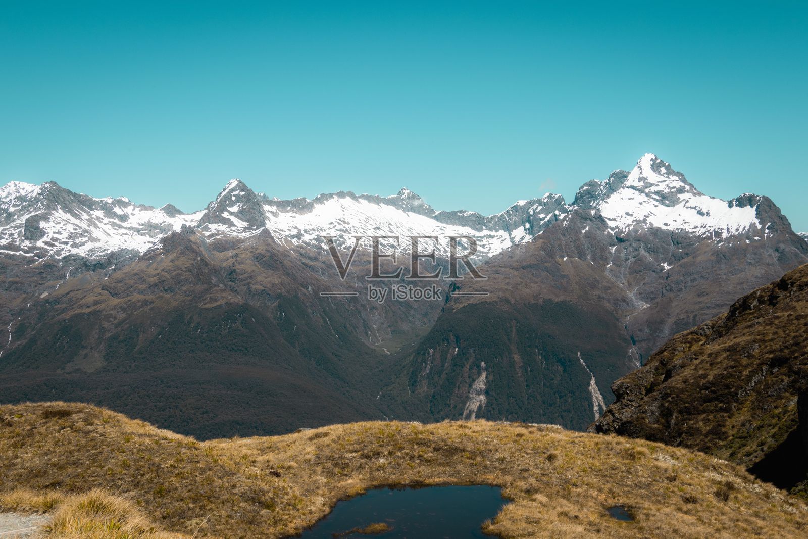 雪山在晴朗的蓝天下，前景是绿草如茵。照片摄影图片