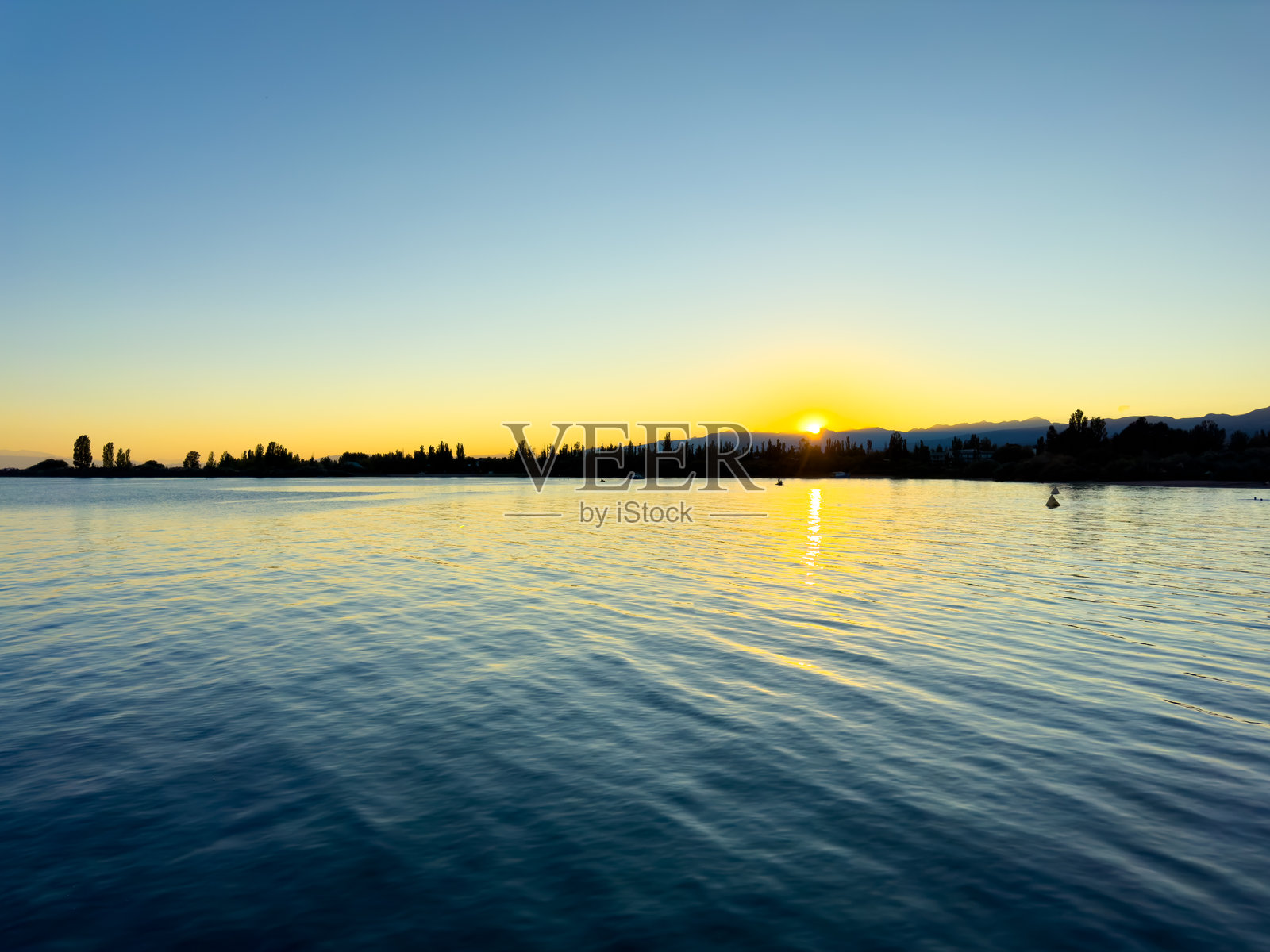 伊塞克湖在多云的天空和背景山脉下。水面平静，映照着天空。清晨时分大自然的宁静与安详。照片摄影图片