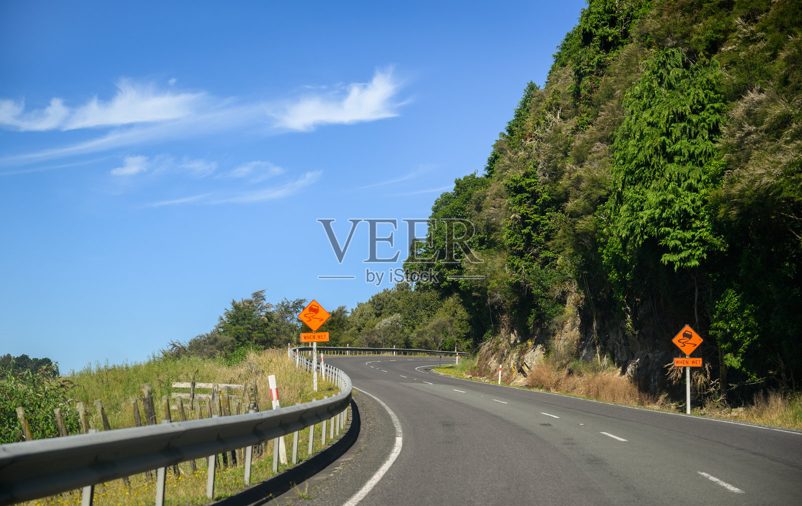 湿滑路段警告标志在蜿蜒的道路上。新西兰北岛。照片摄影图片