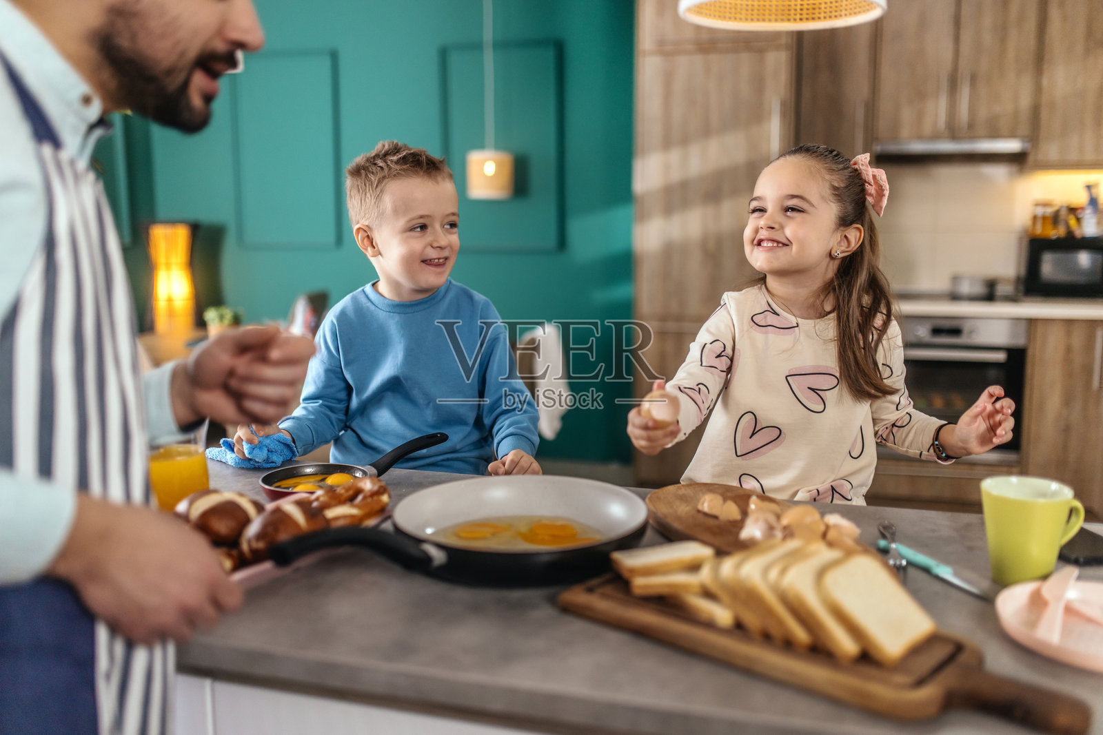 年轻父亲在家里和孩子们一起准备早餐。照片摄影图片
