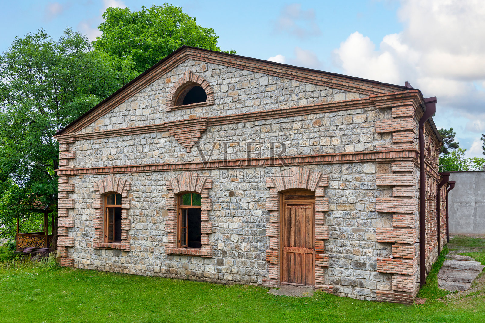 阳光明媚的日子里，古老的石建筑被精美的砖石工艺和绿树环绕照片摄影图片