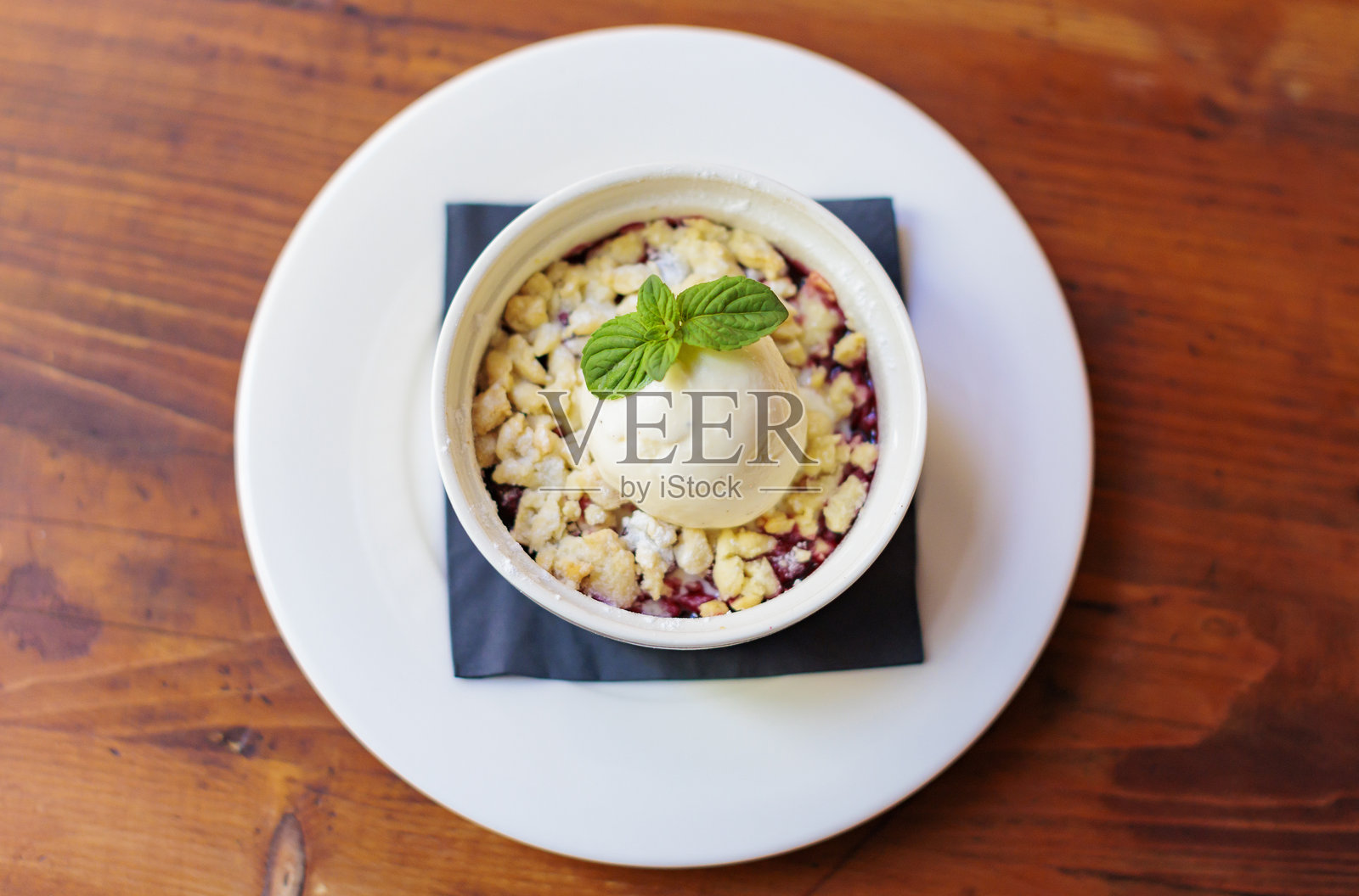 美味的甜点盛在白色的烤 ramekin 中，上面放有新鲜薄荷和奶油香草冰淇淋，底下是水果脆皮。照片摄影图片