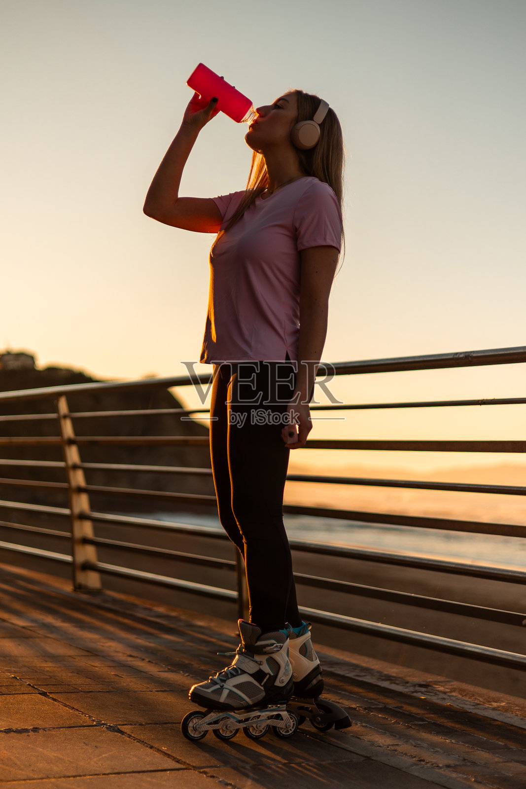 年轻女性在海边日落时滑旱冰喝水照片摄影图片