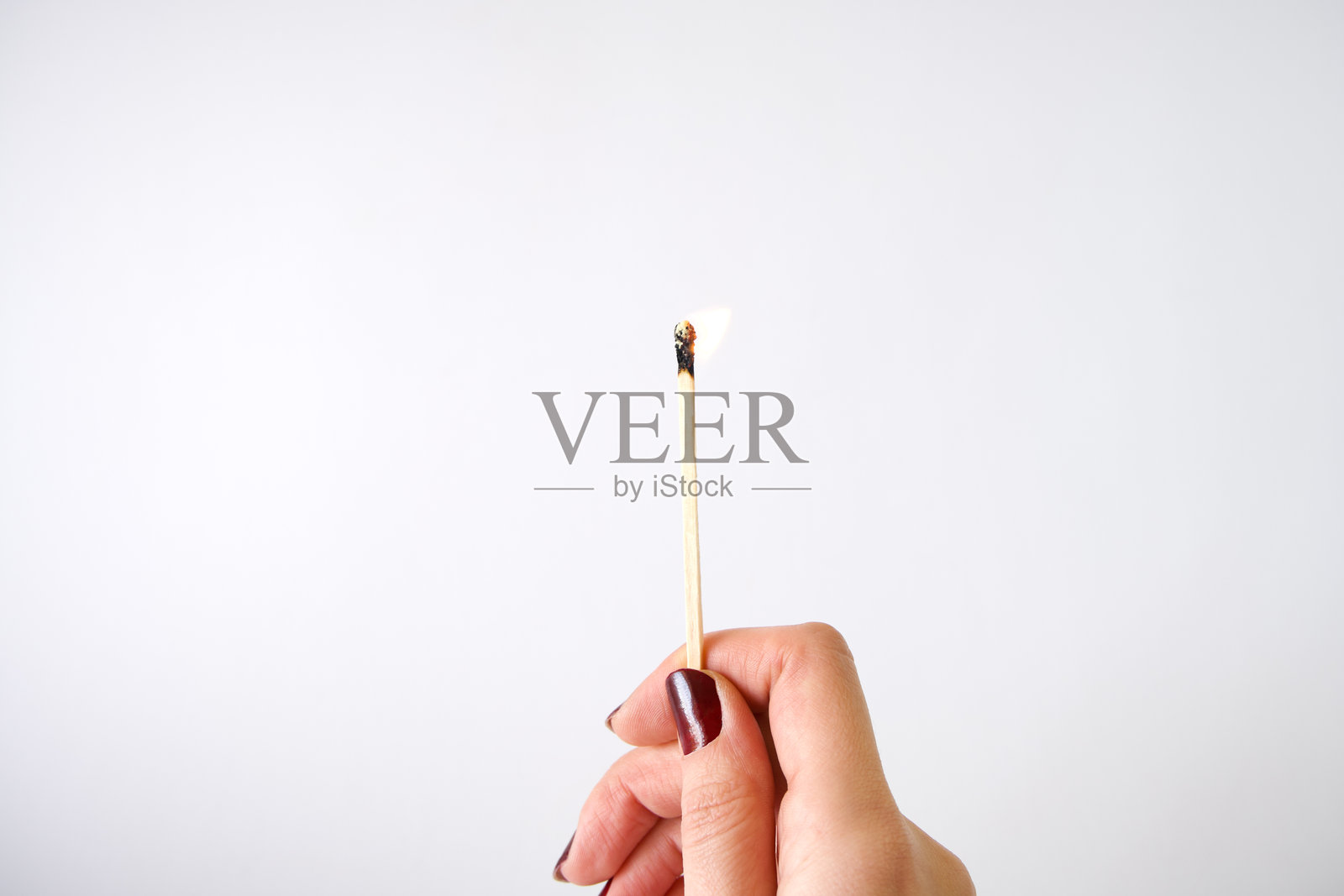 女性手握着燃烧的火柴，背景为灰色照片摄影图片