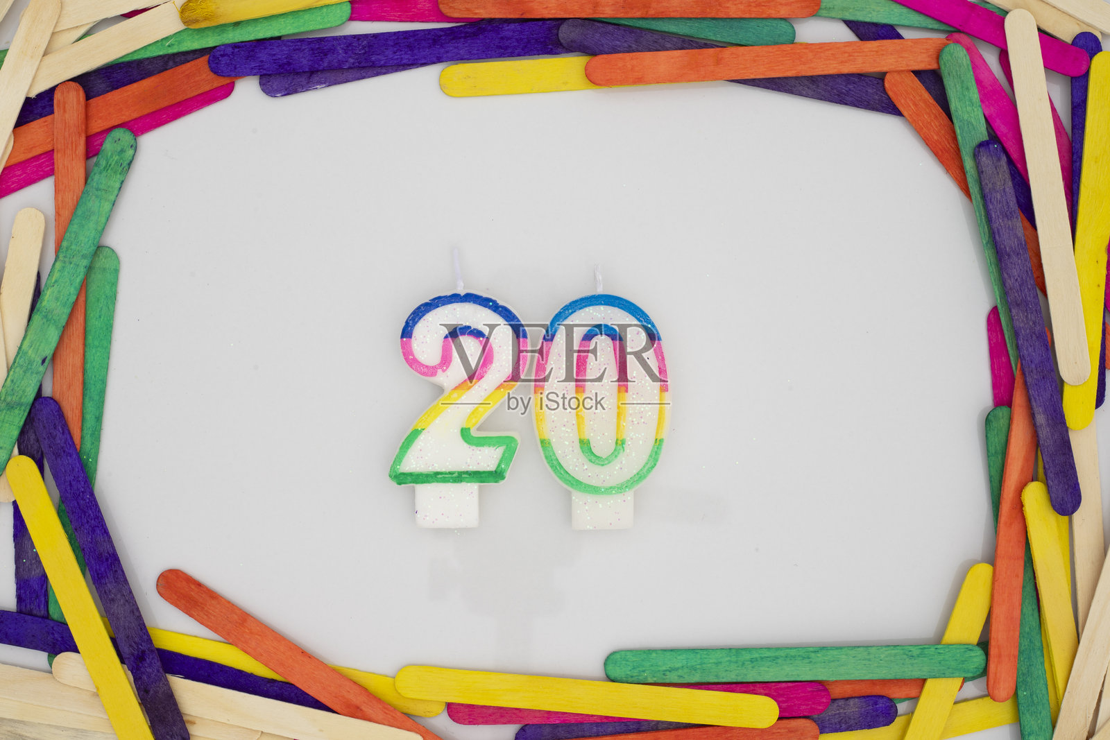 白色背景上，20号形状的生日蜡烛，周围用五彩的冰棍棒框住。照片摄影图片