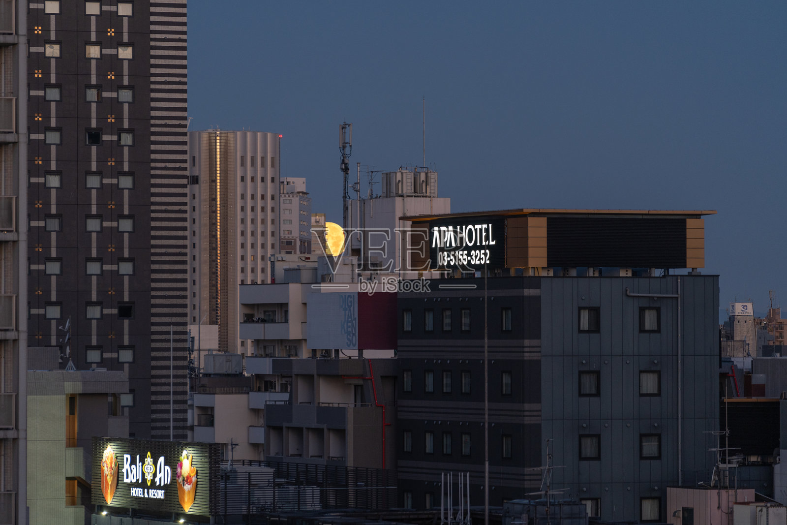 东京高楼大厦背后黄月落下的景象,清晨日出时分,蓝天晴朗。照片摄影图片