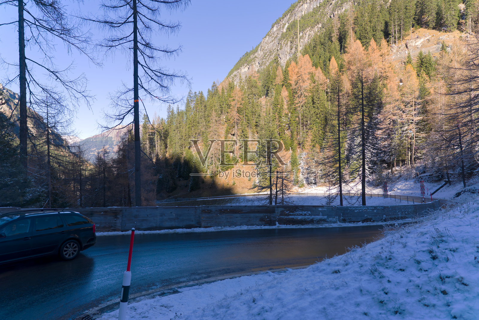 黑色斯柯达汽车在阳光明媚的秋日，位于瑞士山口的特写，周围是秋季林木和雪景。照片摄影图片