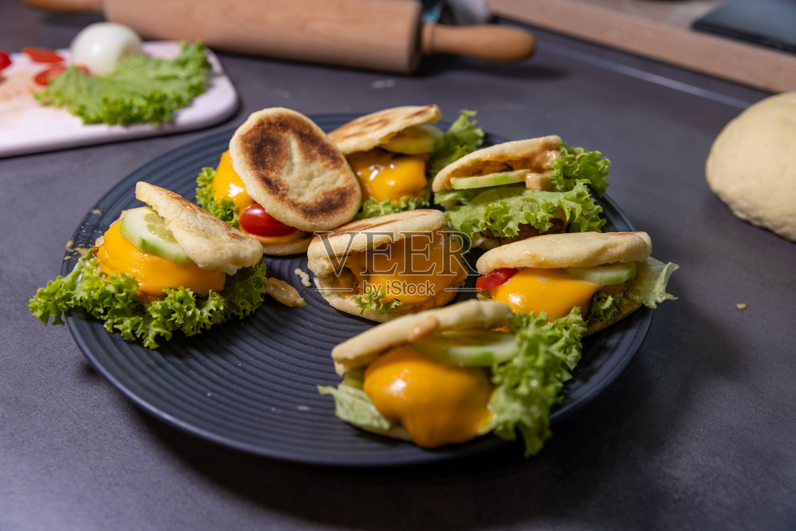 用自制扁面包制作的小三明治，夹有融化的奶酪、新鲜的生菜、黄瓜和樱桃番茄，摆放在黑色盘子上。照片摄影图片