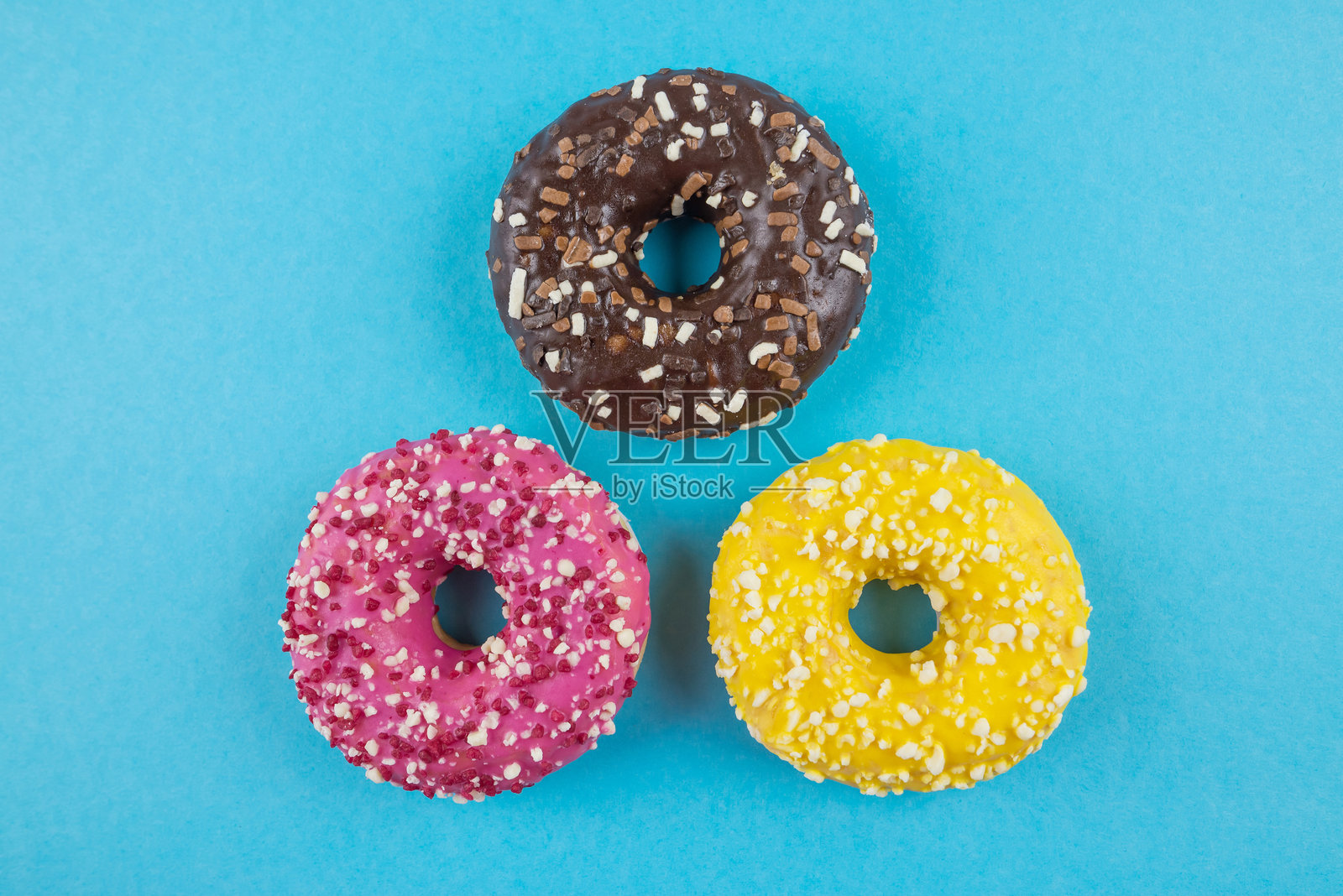三种不同糖霜的甜甜圈在蓝色背景上照片摄影图片
