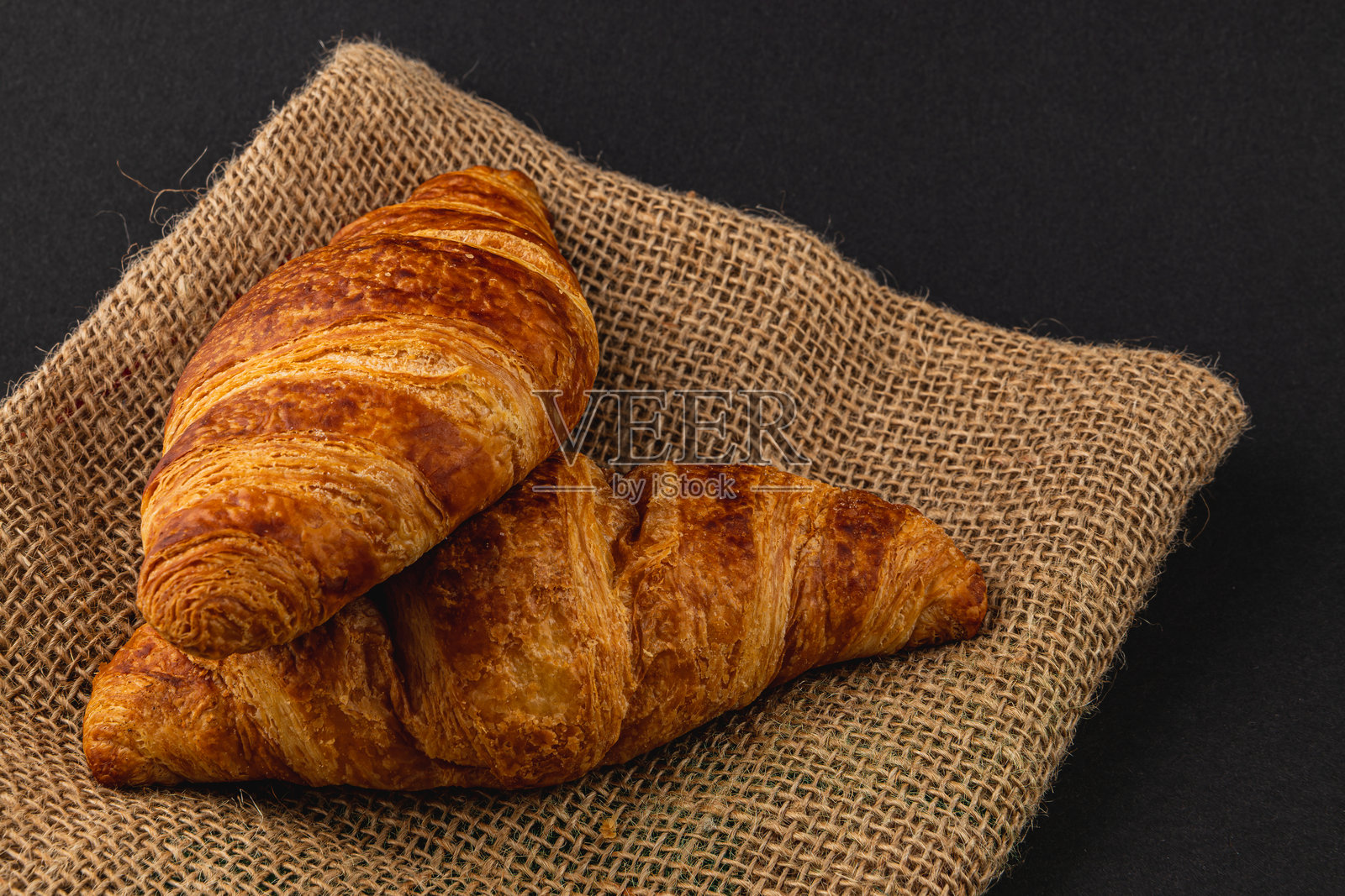 新鲜的金色可颂面包放在黑色背景的麻布上照片摄影图片