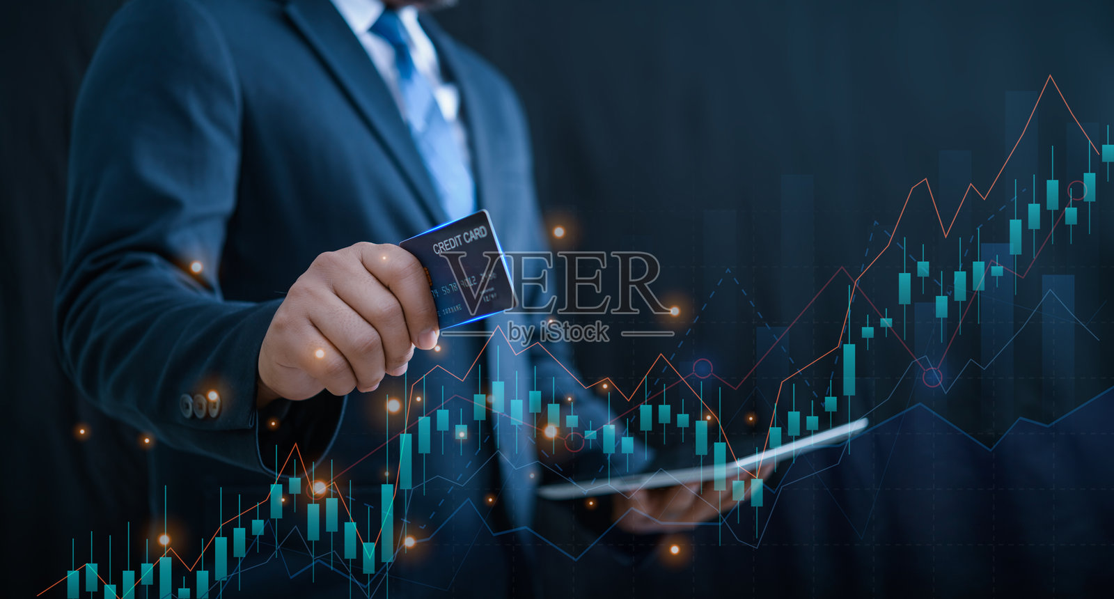 一位聪明的商人手持信用卡和平板电脑，屏幕上显示着市场趋势的图表和图形。照片摄影图片