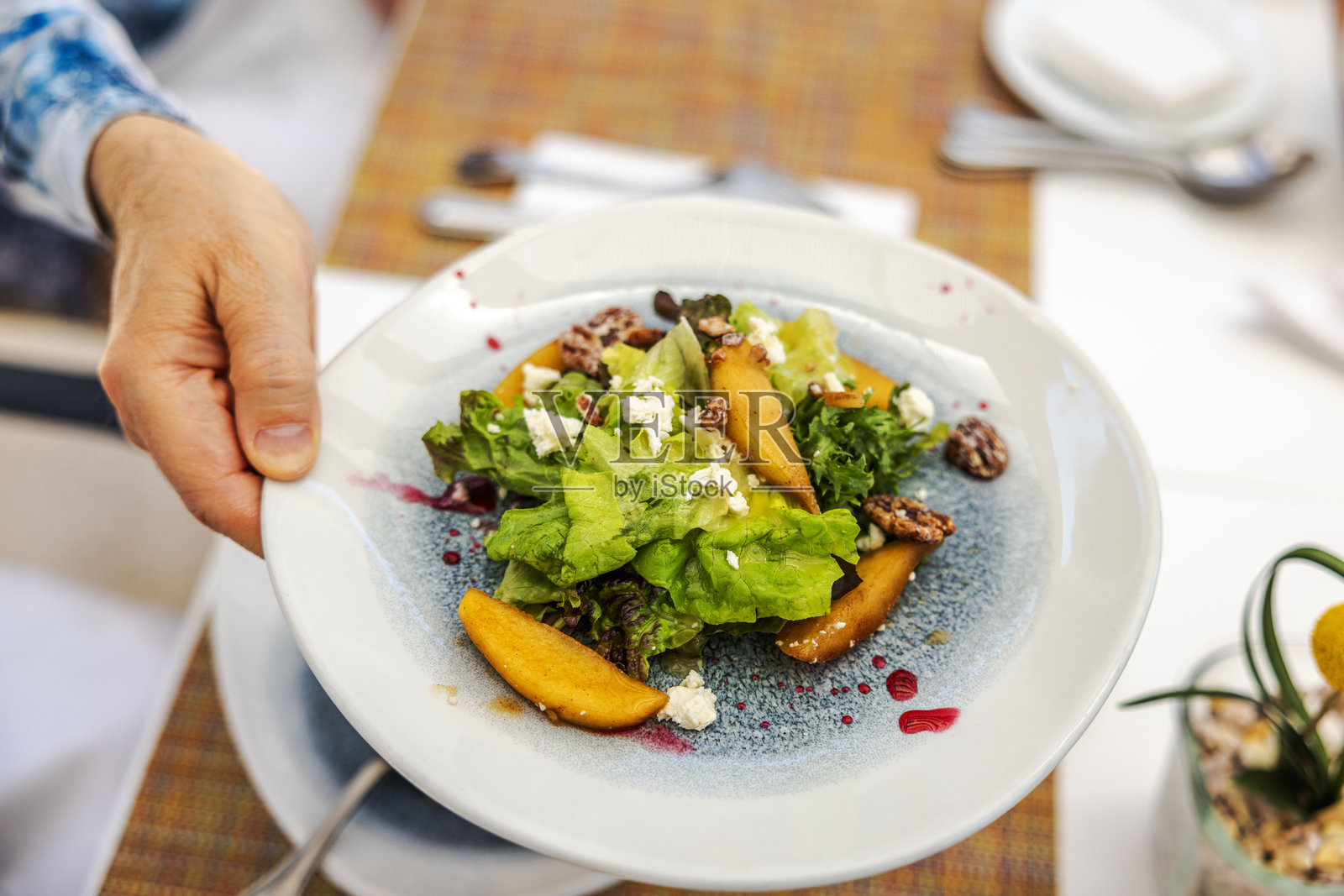 新鲜沙拉特写，包含绿色生菜、桃片、坚果和奶酪，盛放在白色盘子上，淋有酱汁。照片摄影图片