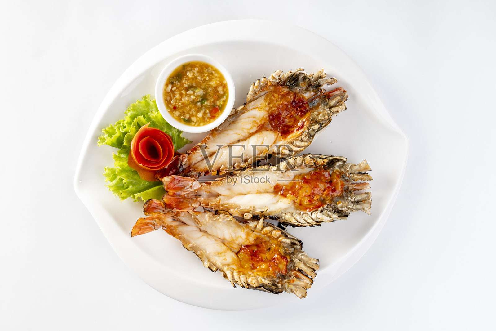 白色背景上，盘子里盛放着烤大河虾，配有泰式海鲜酱。照片摄影图片