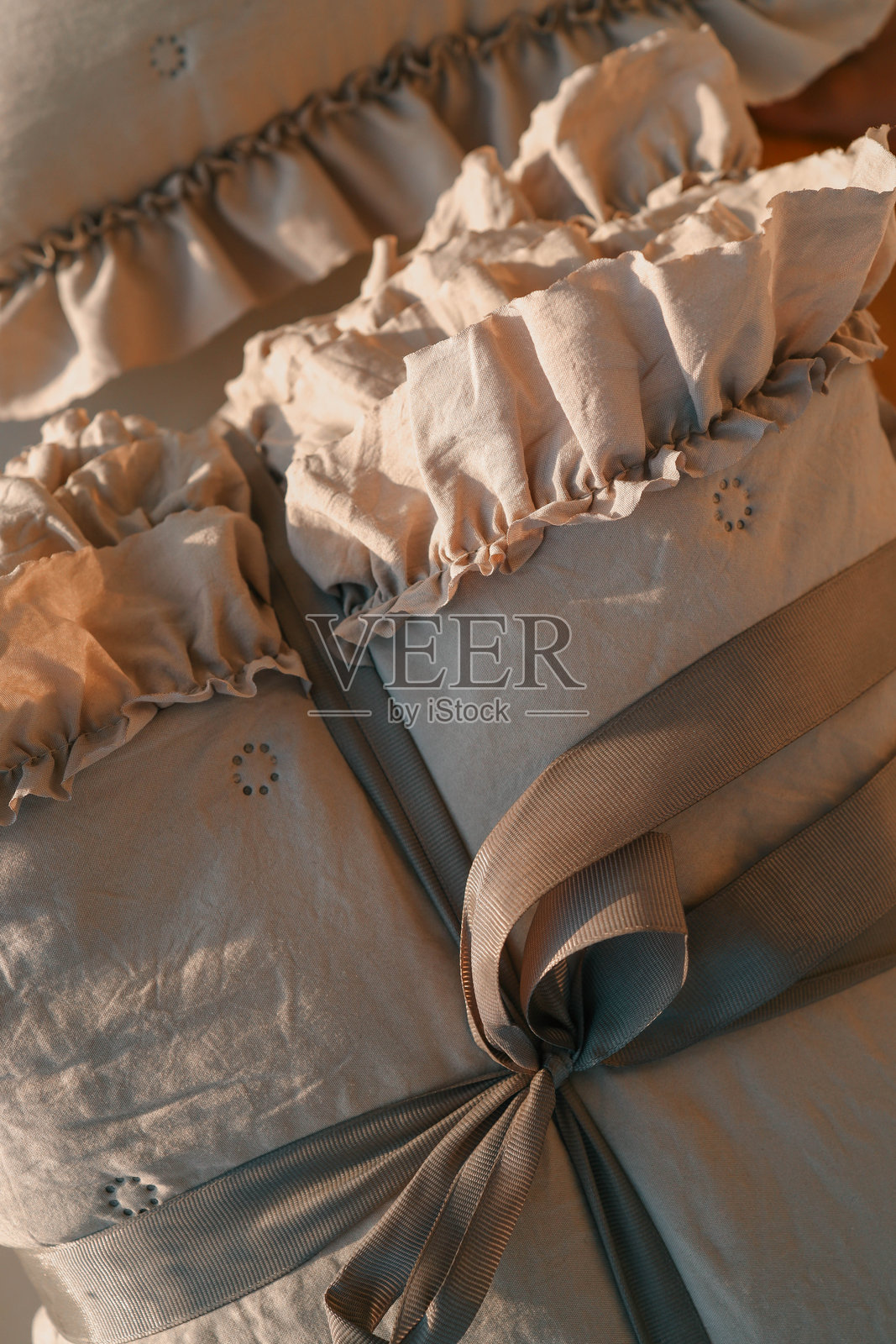 柔和米色的床上用品套件，带有褶边细节，系着灰色丝带，背景为匹配的米色。完美适合舒适、优雅和简约家居装饰主题。照片摄影图片