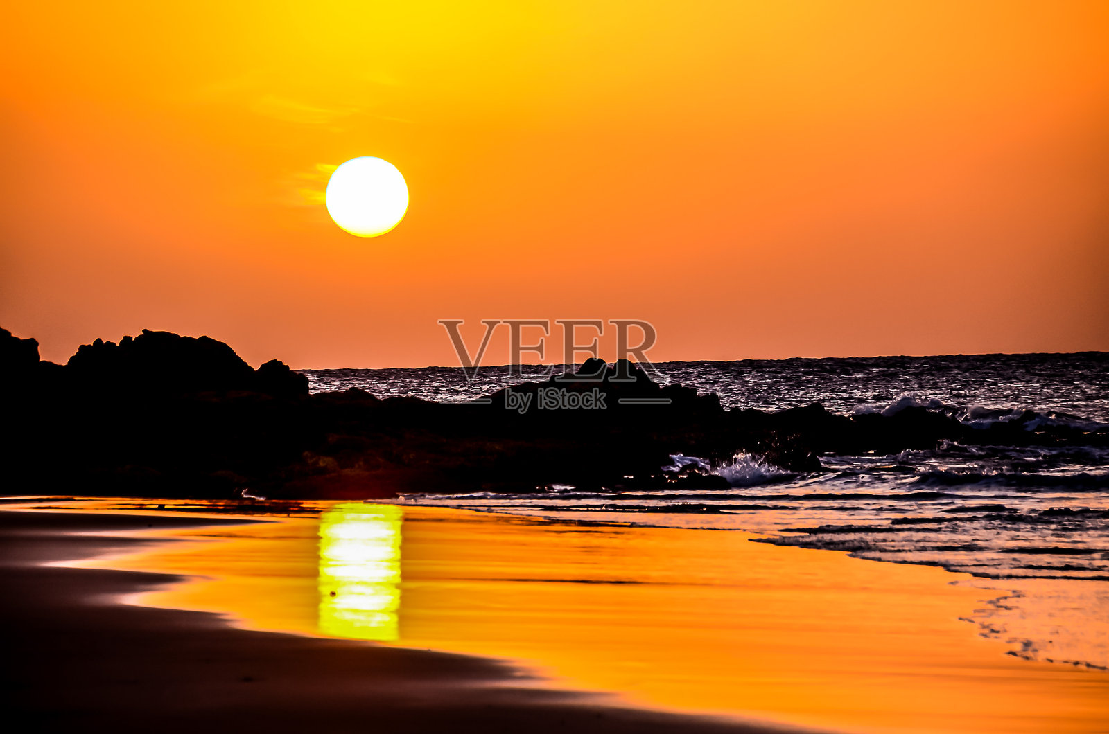 太阳在海面上落下，温暖的光辉洒在岩石和水面上。照片摄影图片