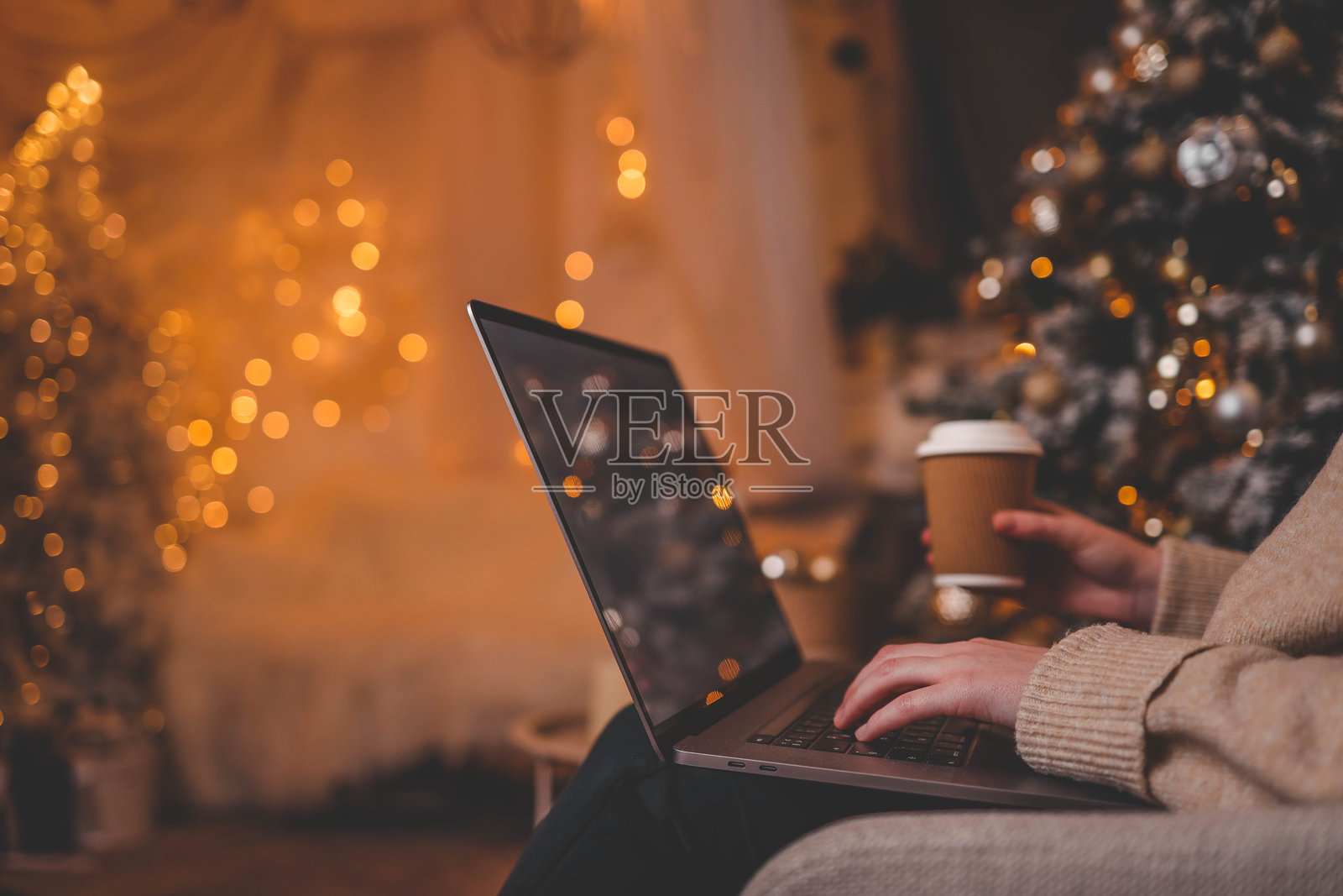 手在笔记本电脑上打字，背景是一棵美丽发光的圣诞树，营造出温馨而节日的室内氛围照片摄影图片