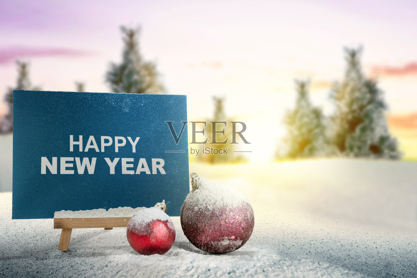 特写镜头展示了圣诞球和写有“新年快乐”的信封，背景是雪地，放置在木质画架上。照片摄影图片