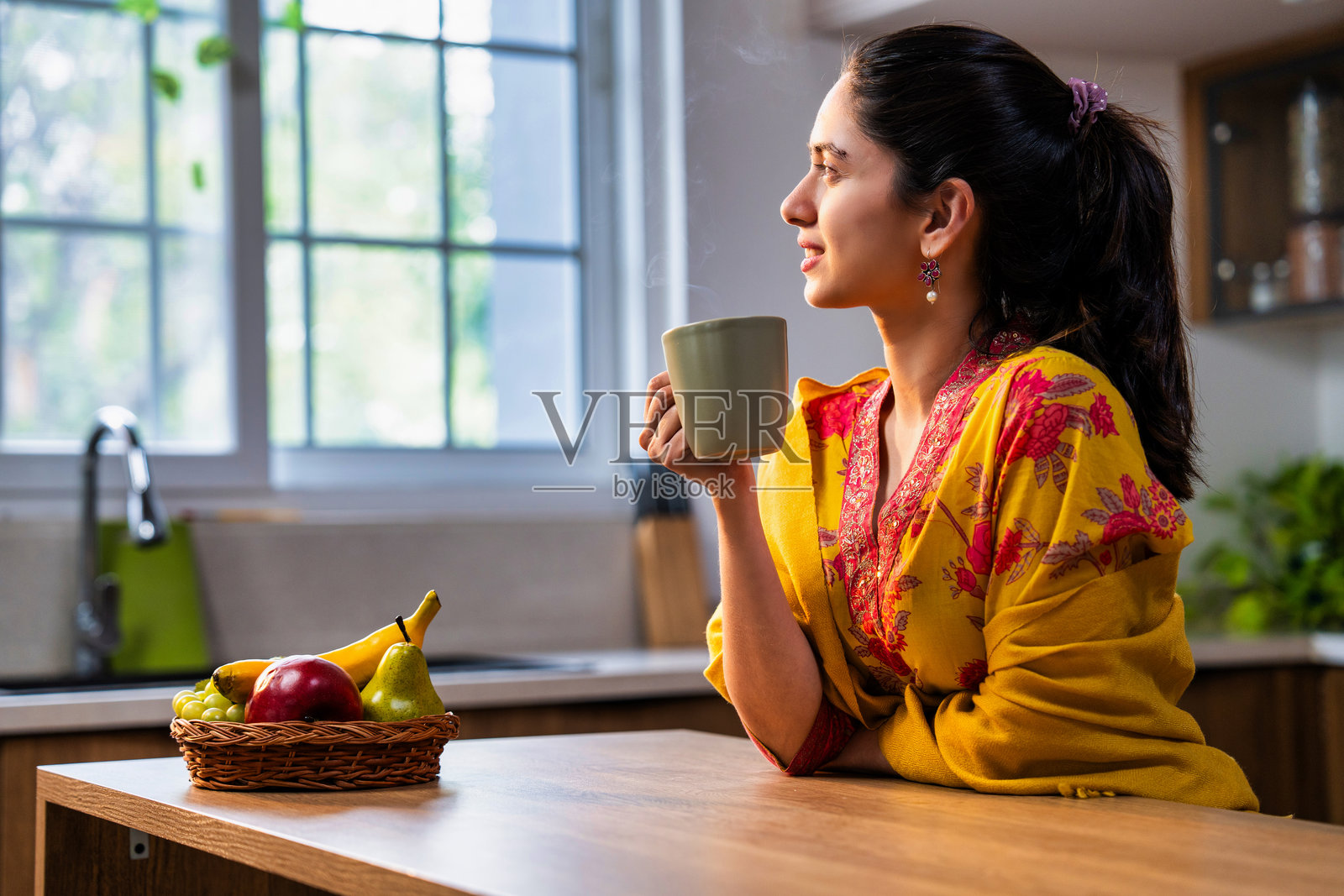 漂亮的年轻印度女孩穿着沙尔瓦尔卡米兹，在晨光中享受热咖啡。照片摄影图片