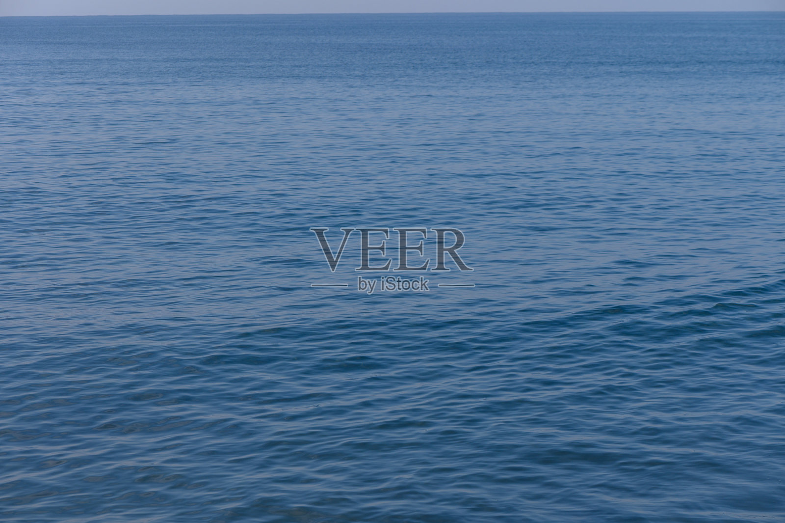 平静的蓝色海洋在晴朗的天空下无尽延展，温柔的波浪轻轻拍打着海岸。照片摄影图片