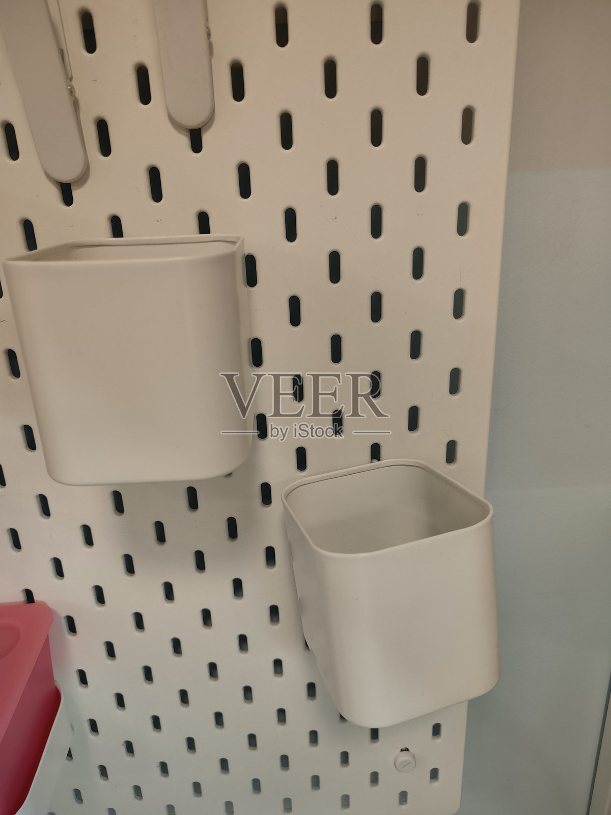 一个白色塑料桶挂在墙上，带有黑色孔洞。照片摄影图片