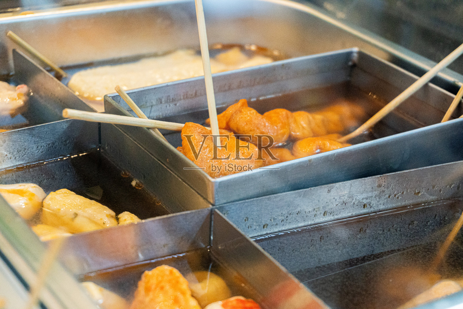 金属容器中各种关东煮食材的特写，木签插着，正在汤汁中炖煮。照片摄影图片