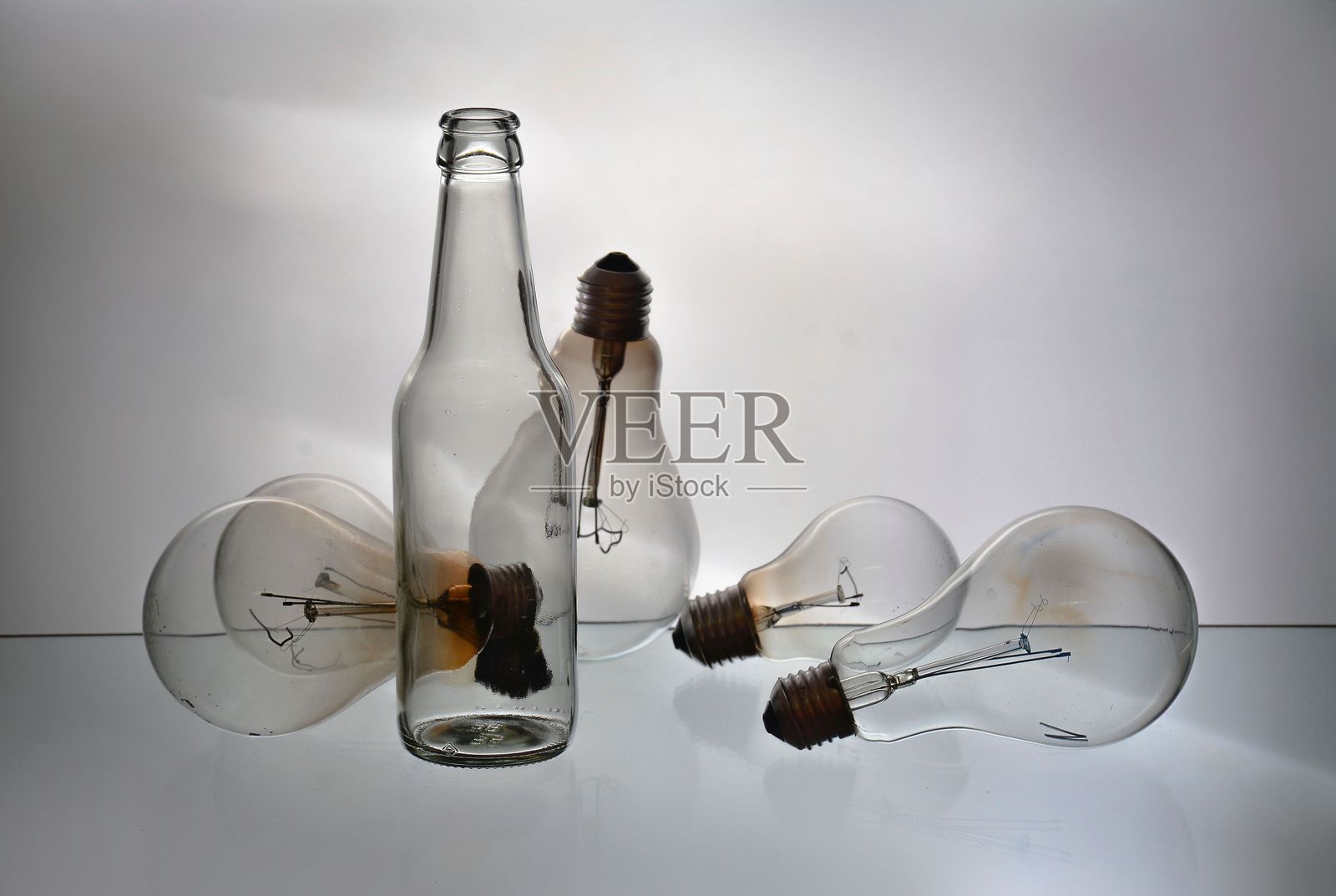 随机排列的灯泡和一个瓶子放在白色背景的玻璃桌上。照片摄影图片