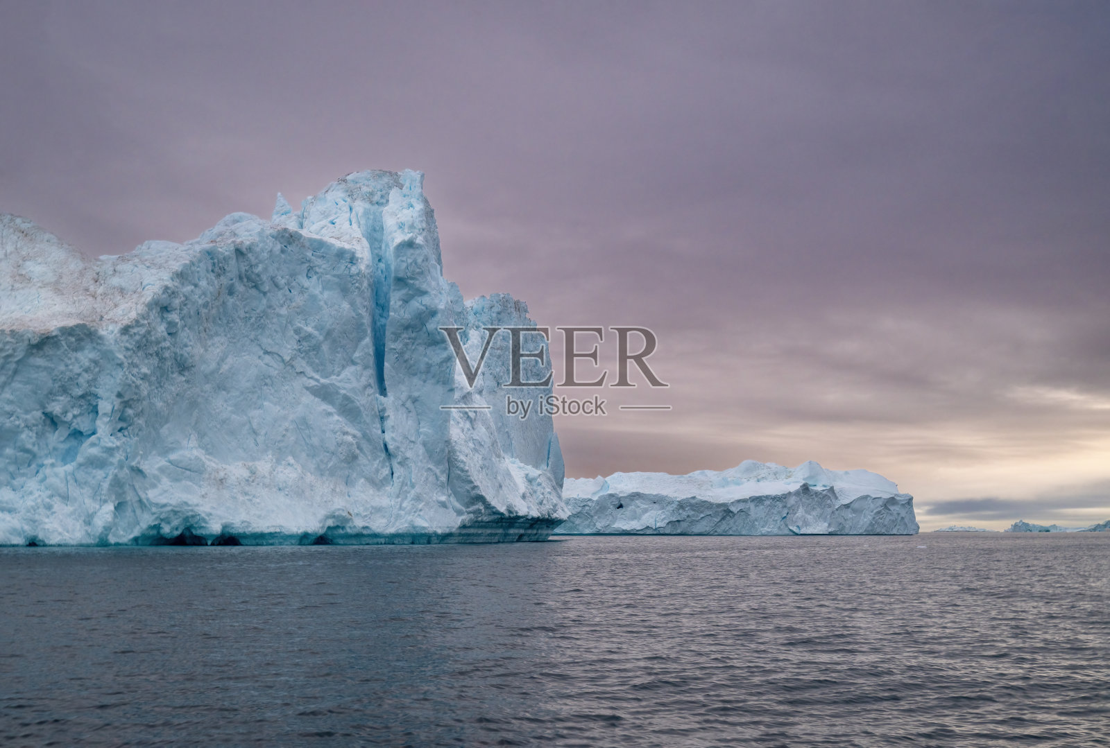 在格林兰的伊卢利萨特，午夜极昼的太阳季节，冰山在恶劣天气中漂浮，笼罩在黄昏的雾气中。照片摄影图片