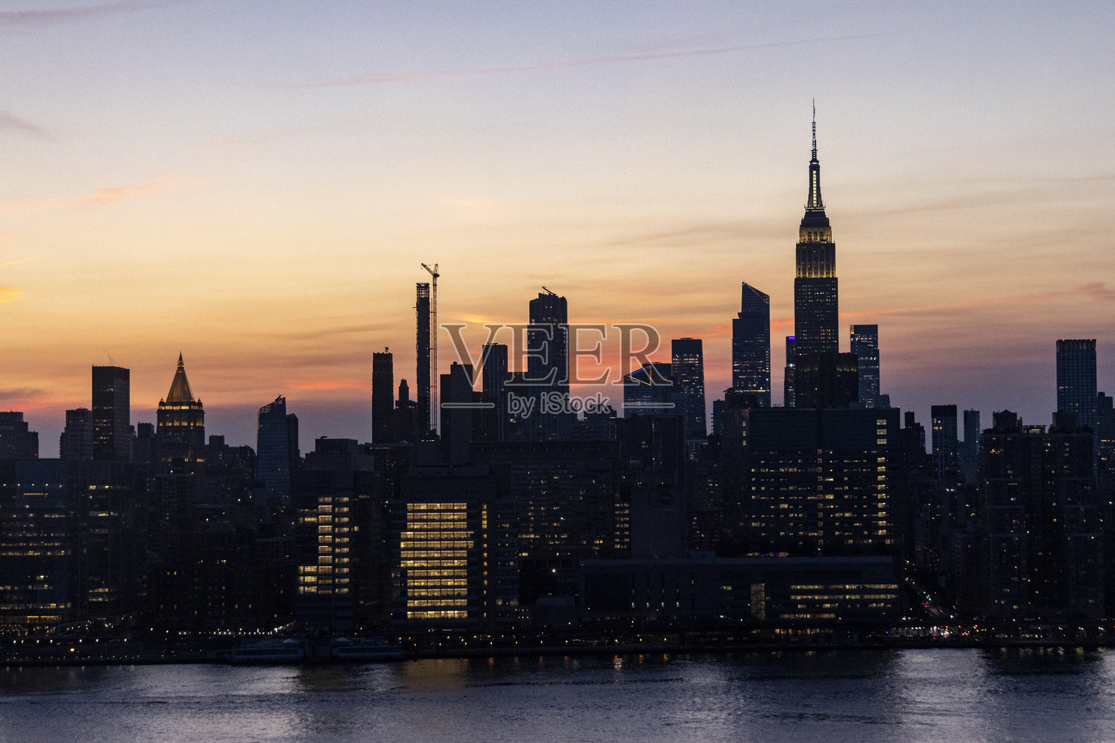 令人惊叹的日落映照在纽约市天际线，突显标志性建筑和水面的倒影照片摄影图片