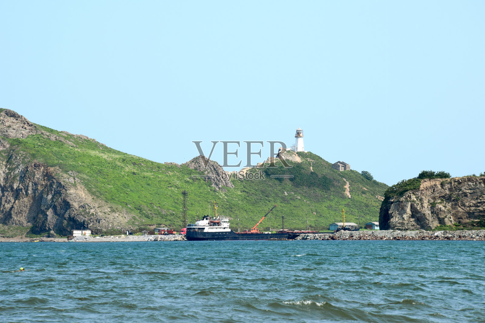 货船停靠在岸边，背景是一座山和一座灯塔。照片摄影图片