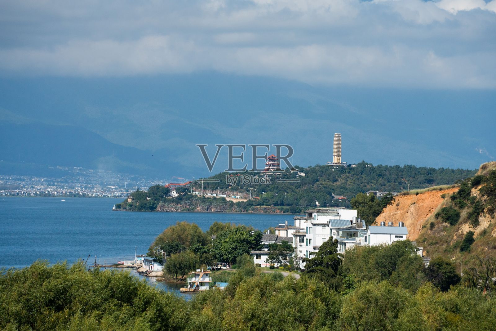 海滨小镇，背靠群山，天空多云。照片摄影图片
