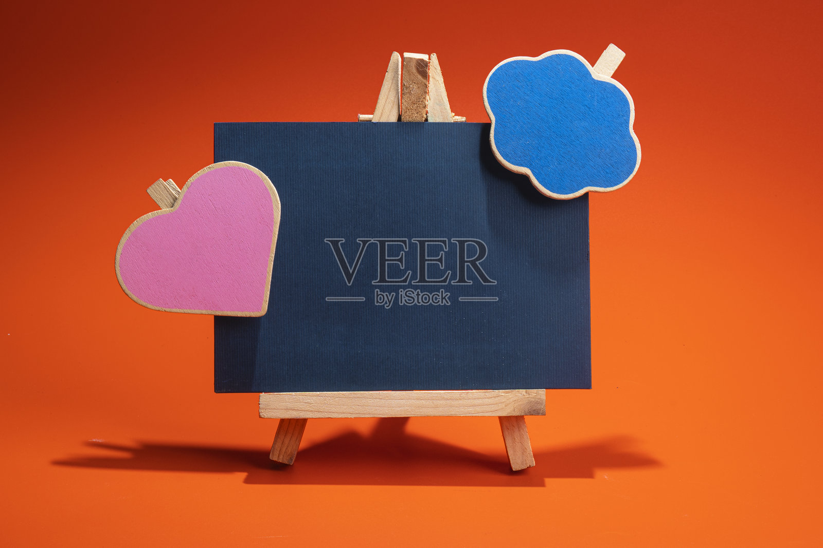 黑纸上的粉色心形和蓝色云朵，放在木质画架上，背景为彩色。照片摄影图片