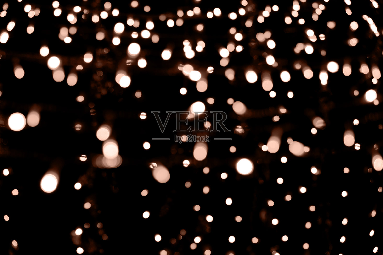 模糊的花环灯光在黑暗背景上。节日的圣诞和新年背景。柔和的焦点。图像调色为2024年的年度颜色 - 桃子绒。照片摄影图片