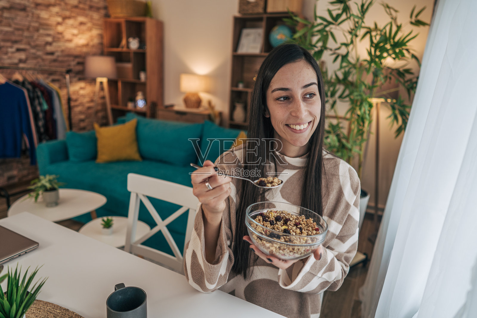 一位长直发的女性坐在餐桌旁，享用一碗麦片。照片摄影图片