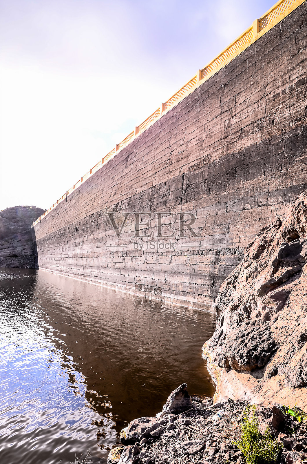 一面巨大的岩石和土壤墙壁，前面有一片水域照片摄影图片