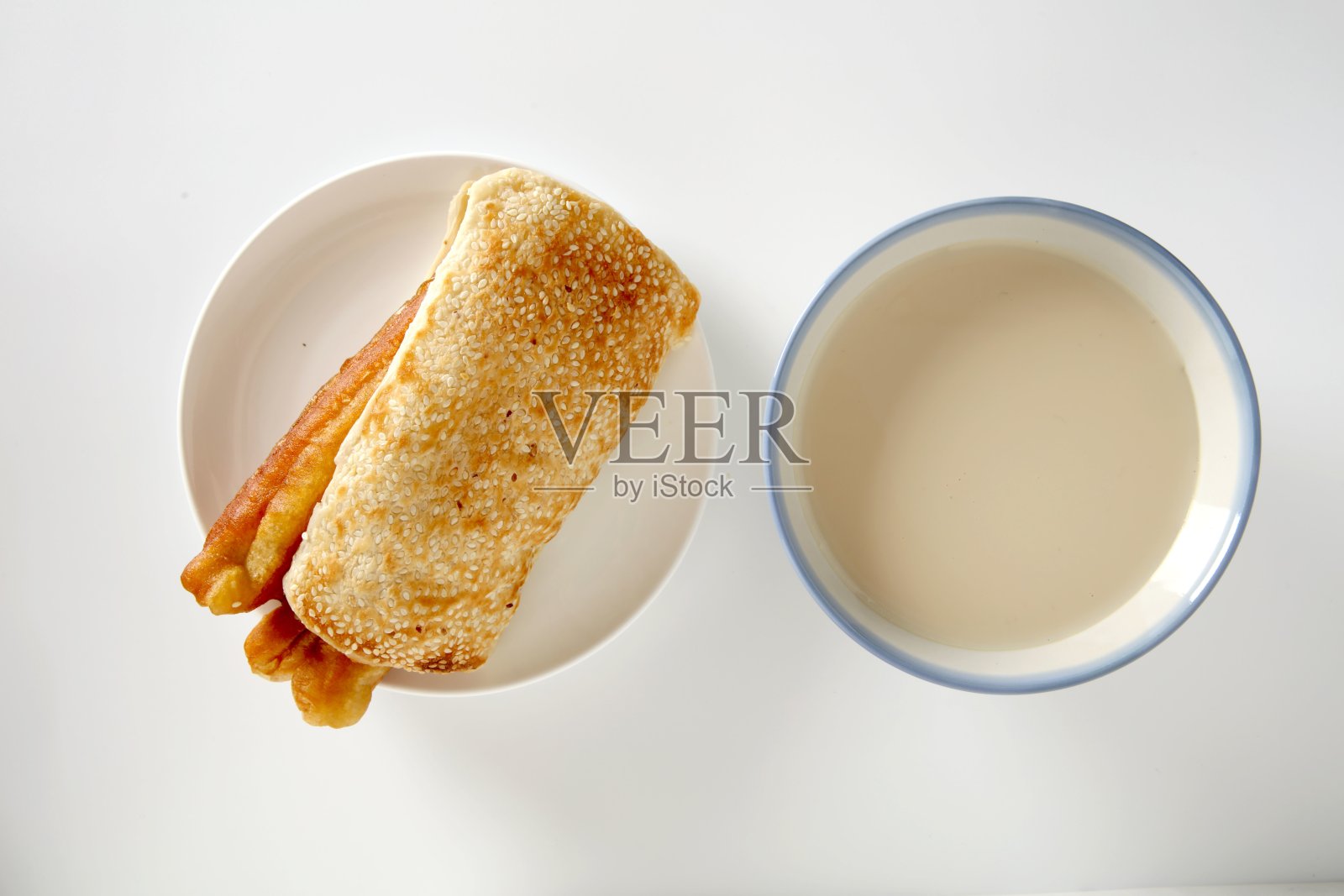 从上方俯视的中国早餐：芝麻饼和油条，配一碗豆浆。照片摄影图片