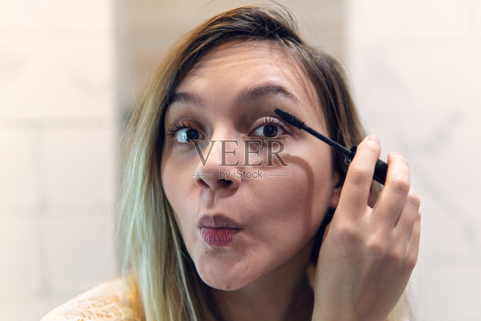 金发女孩在家中镜子前涂抹睫毛膏。特写镜头，选择性对焦。照片摄影图片