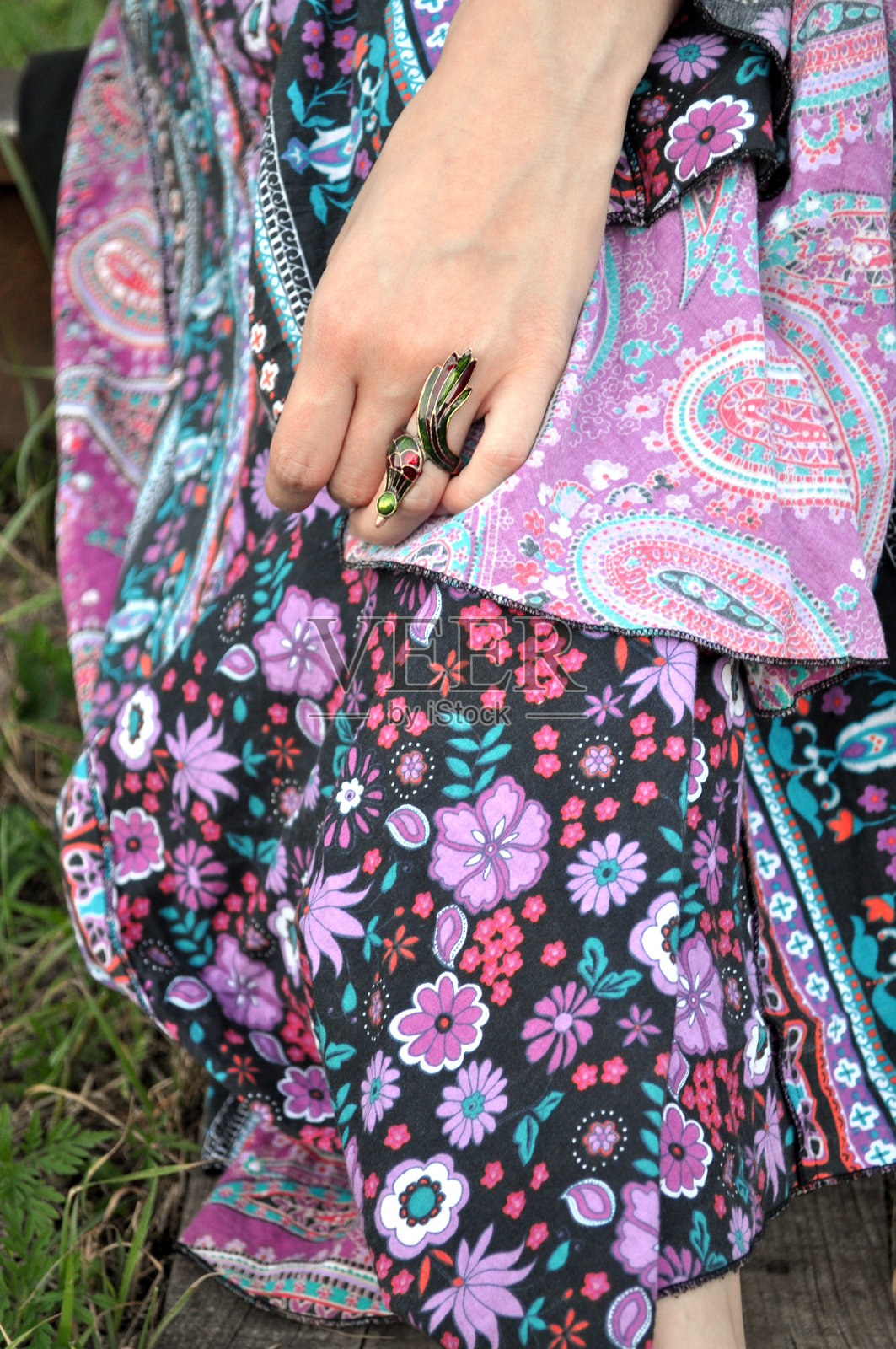 女孩手上戴着一枚带有彩色鸟设计的戒指，背景是鲜艳花卉图案的衣物。照片摄影图片