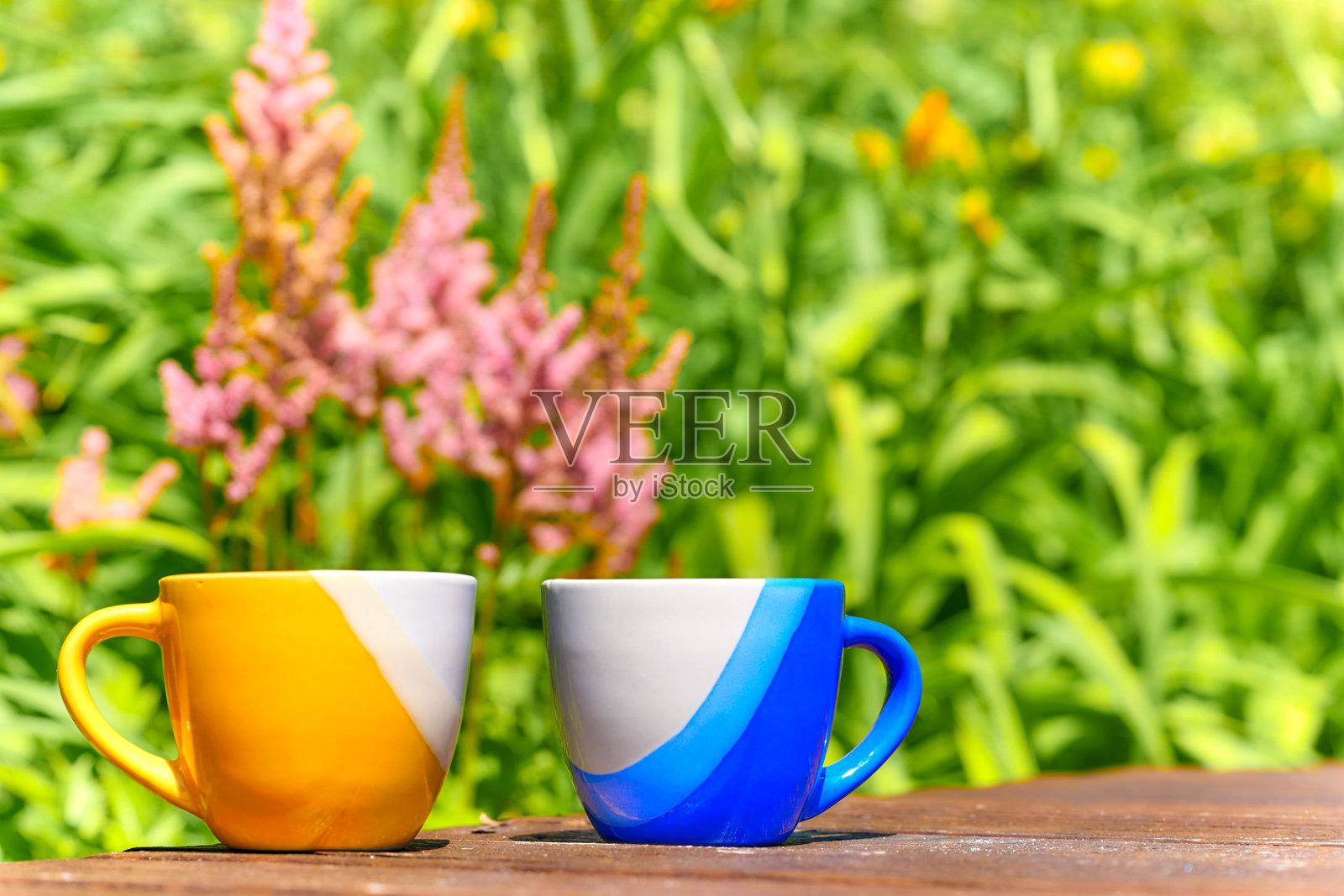 茶歇。咖啡时间。盛开的花园中，蓝色和黄色的杯子放在木桌上。照片摄影图片