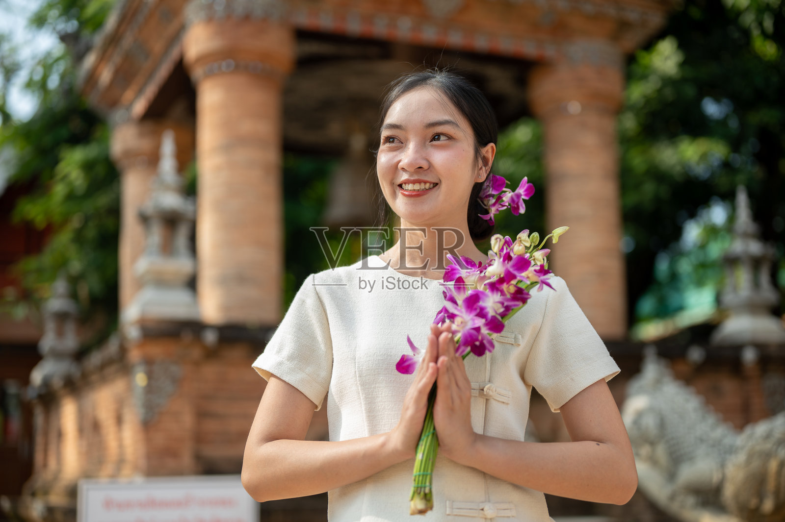 一位迷人的亚洲女性在寺庙户外，双手合十，手中捧着一朵花。照片摄影图片